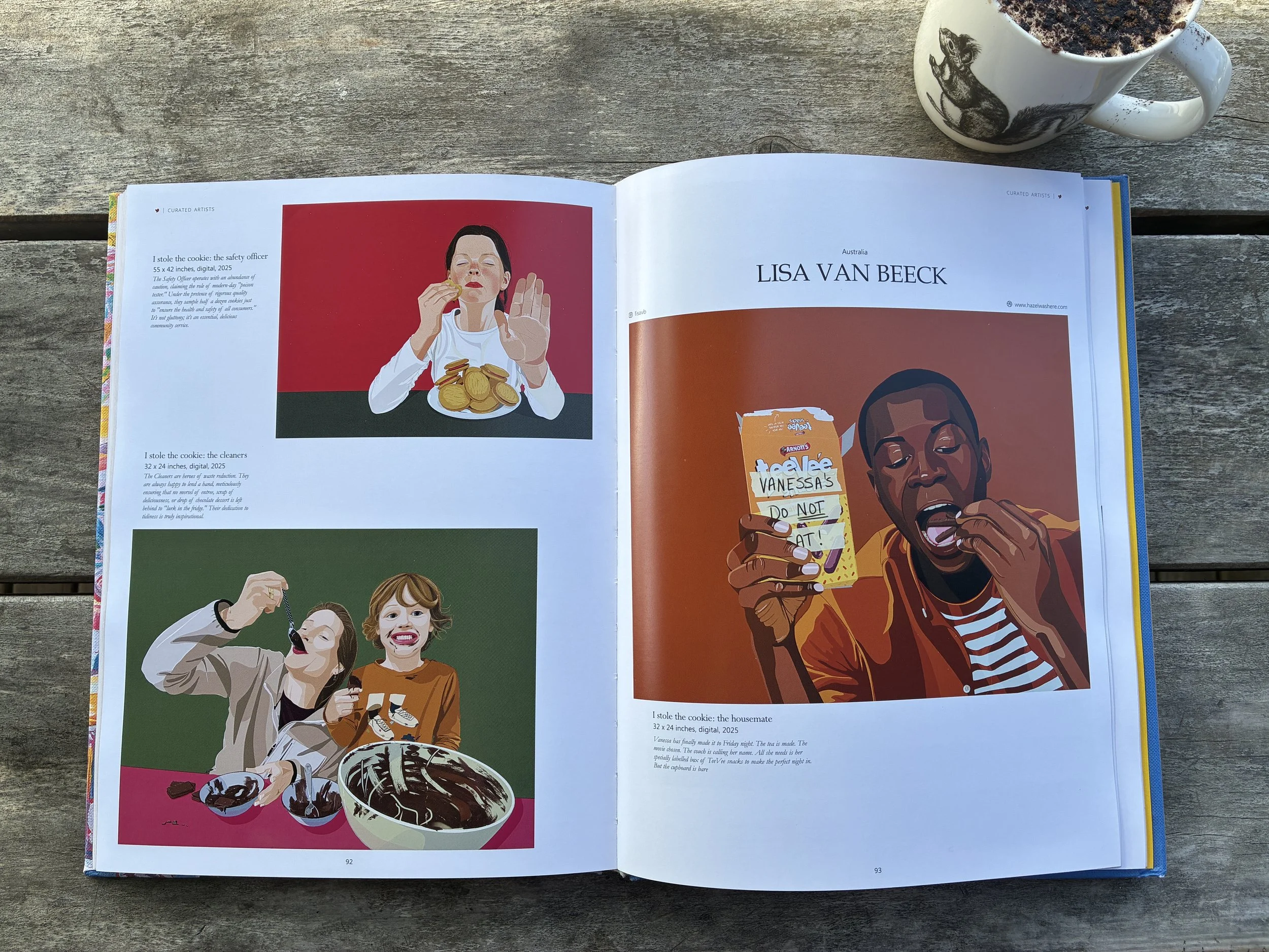Open magazine on a wooden surface with illustrations of people enjoying cookies and snacks, and a mug with a cat design and chocolate drink.