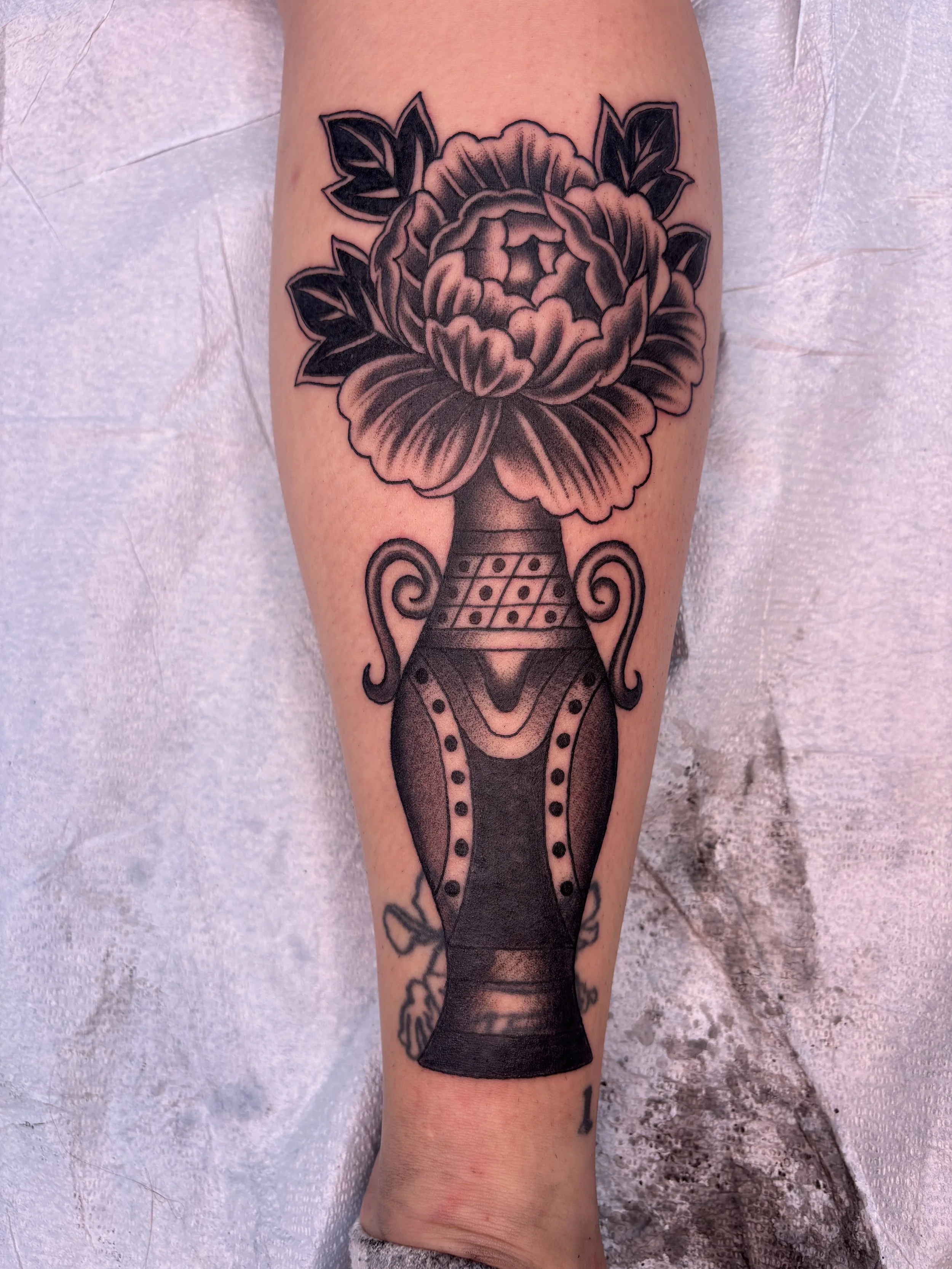 Black and gray tattoo of a bouquet of flowers in a decorative vase on a person's forearm.