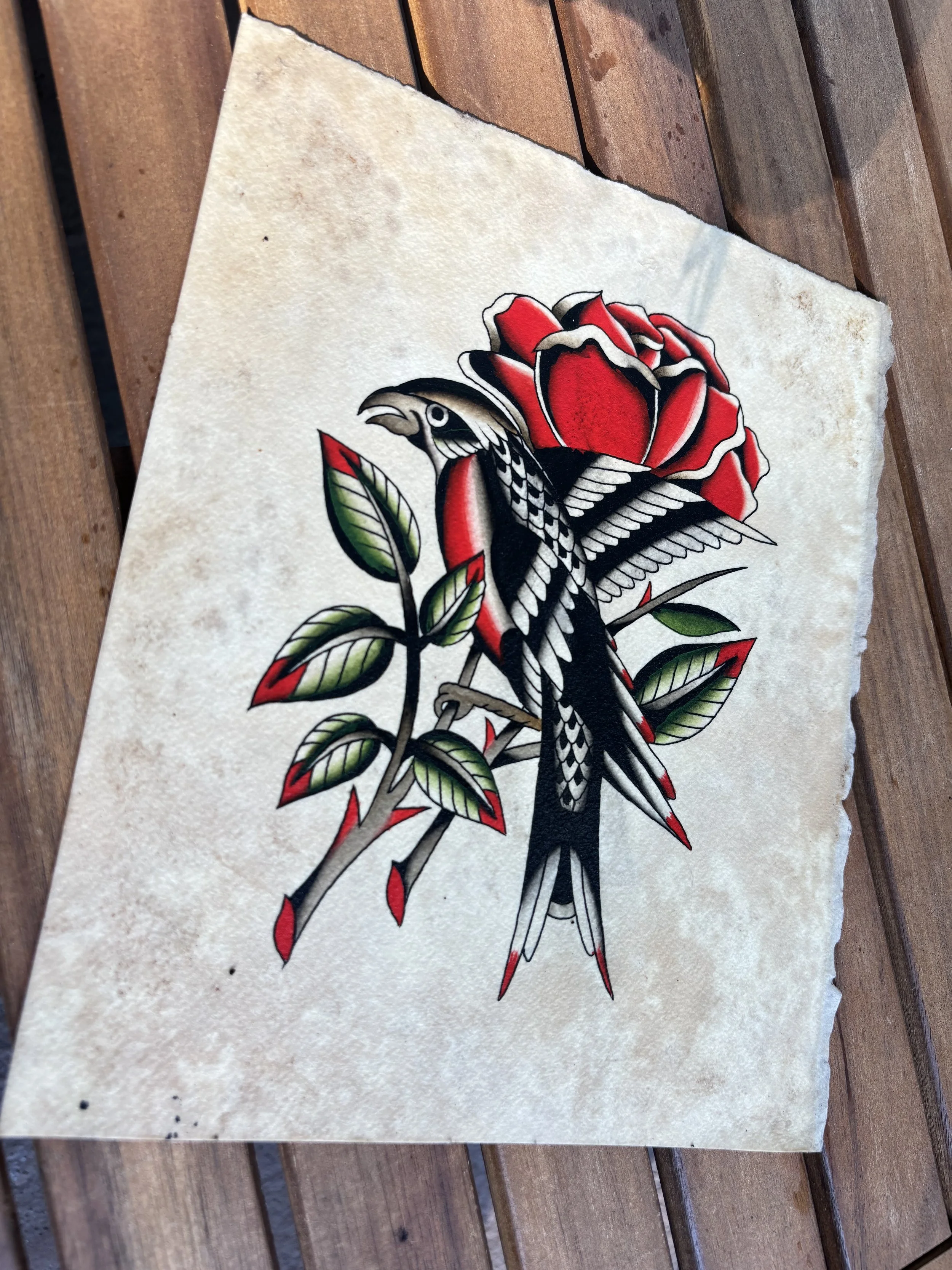 Tattoo-style illustration of a bird perched on a branch with a red rose, leaves, and thorns, on textured beige paper.