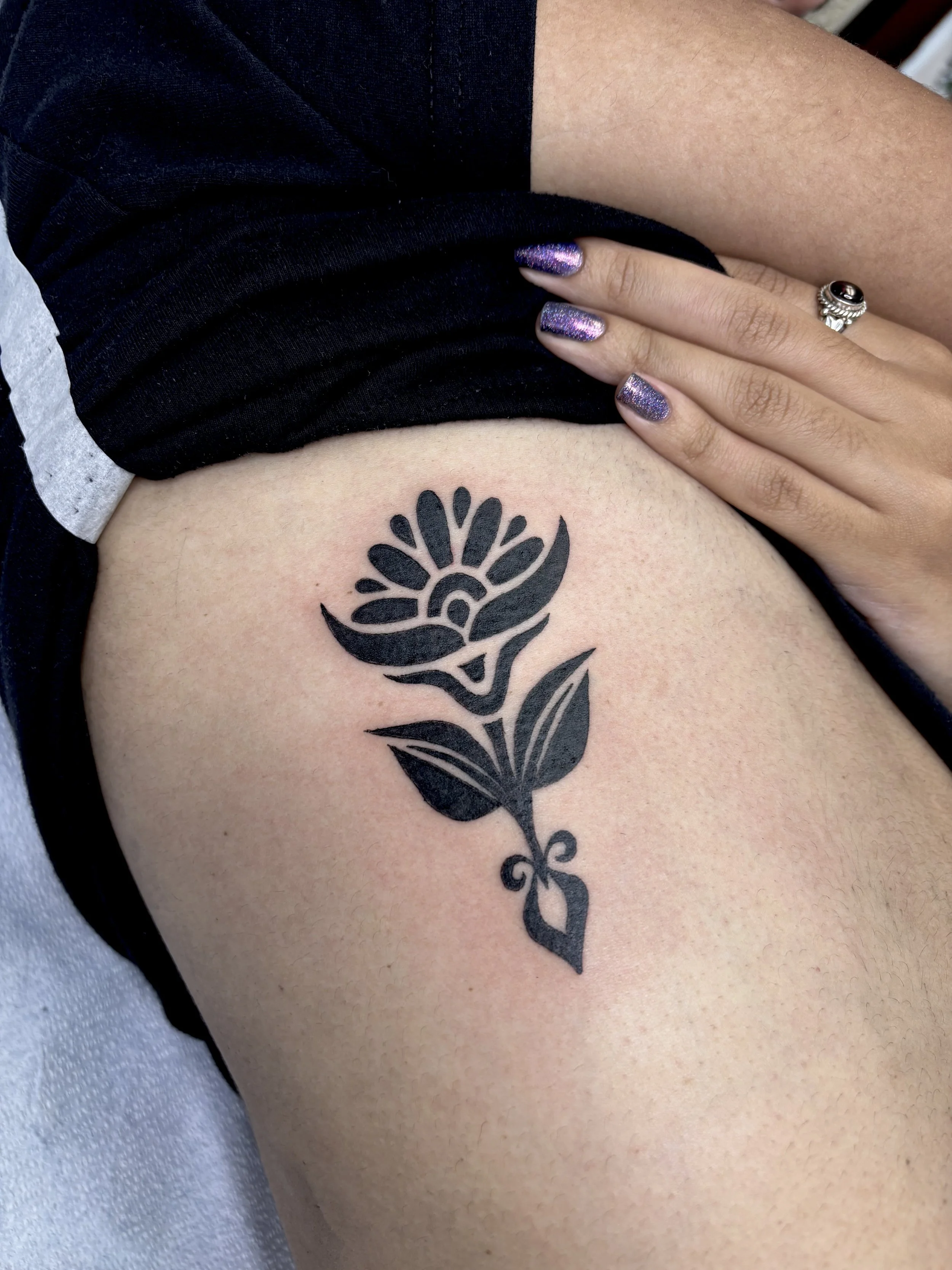 A black floral tattoo on a person's upper thigh.