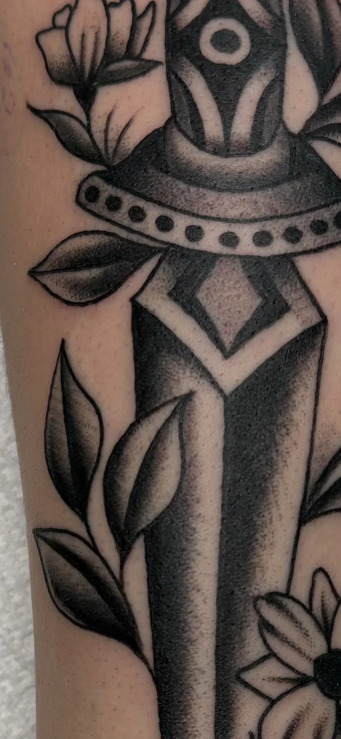 Close-up of a black and gray tattoo featuring a stylized rose, leaves, geometric shapes, and a daisy flower.