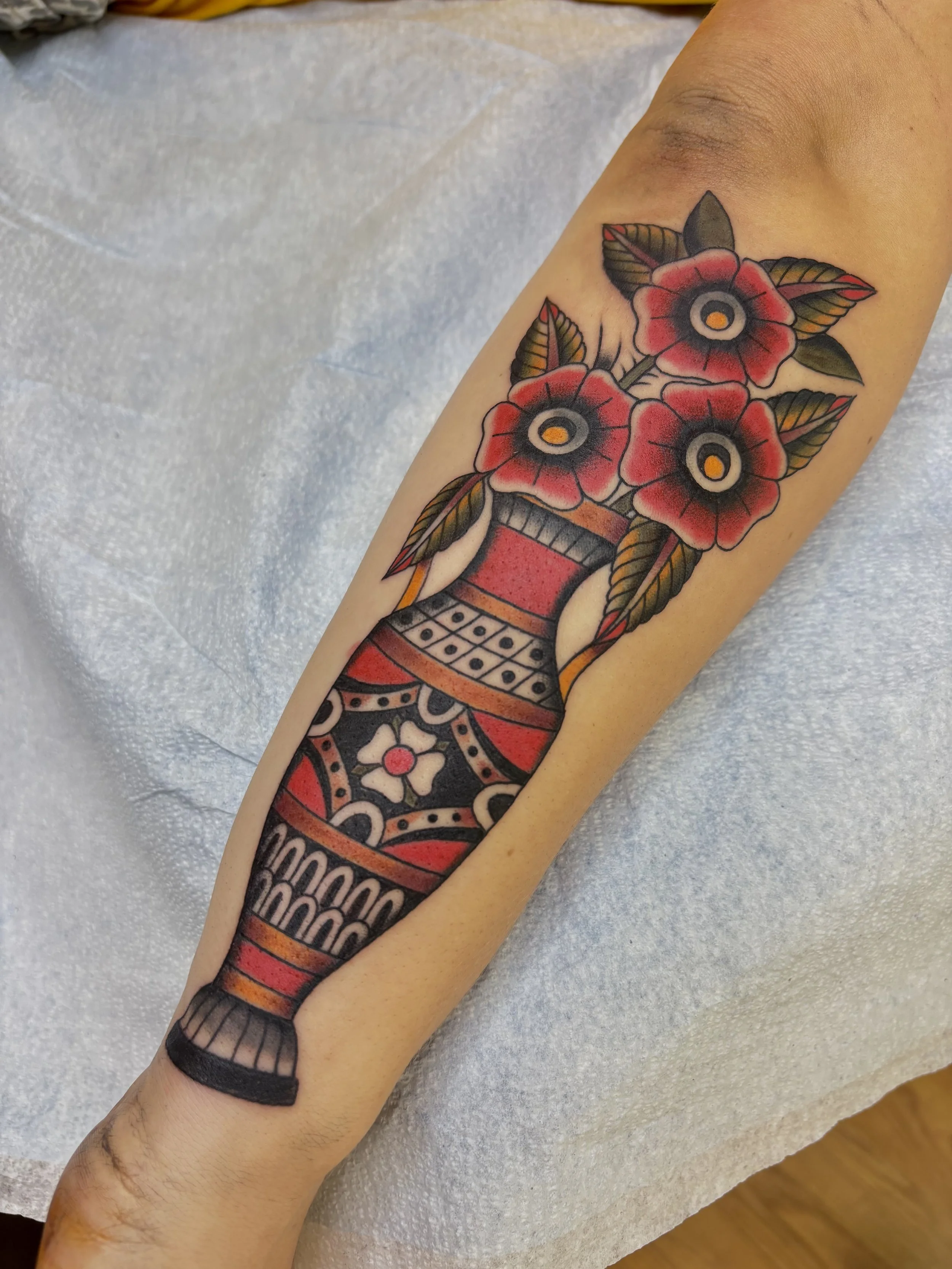 Tattoo of three red flowers in a black vase on a person's forearm.
