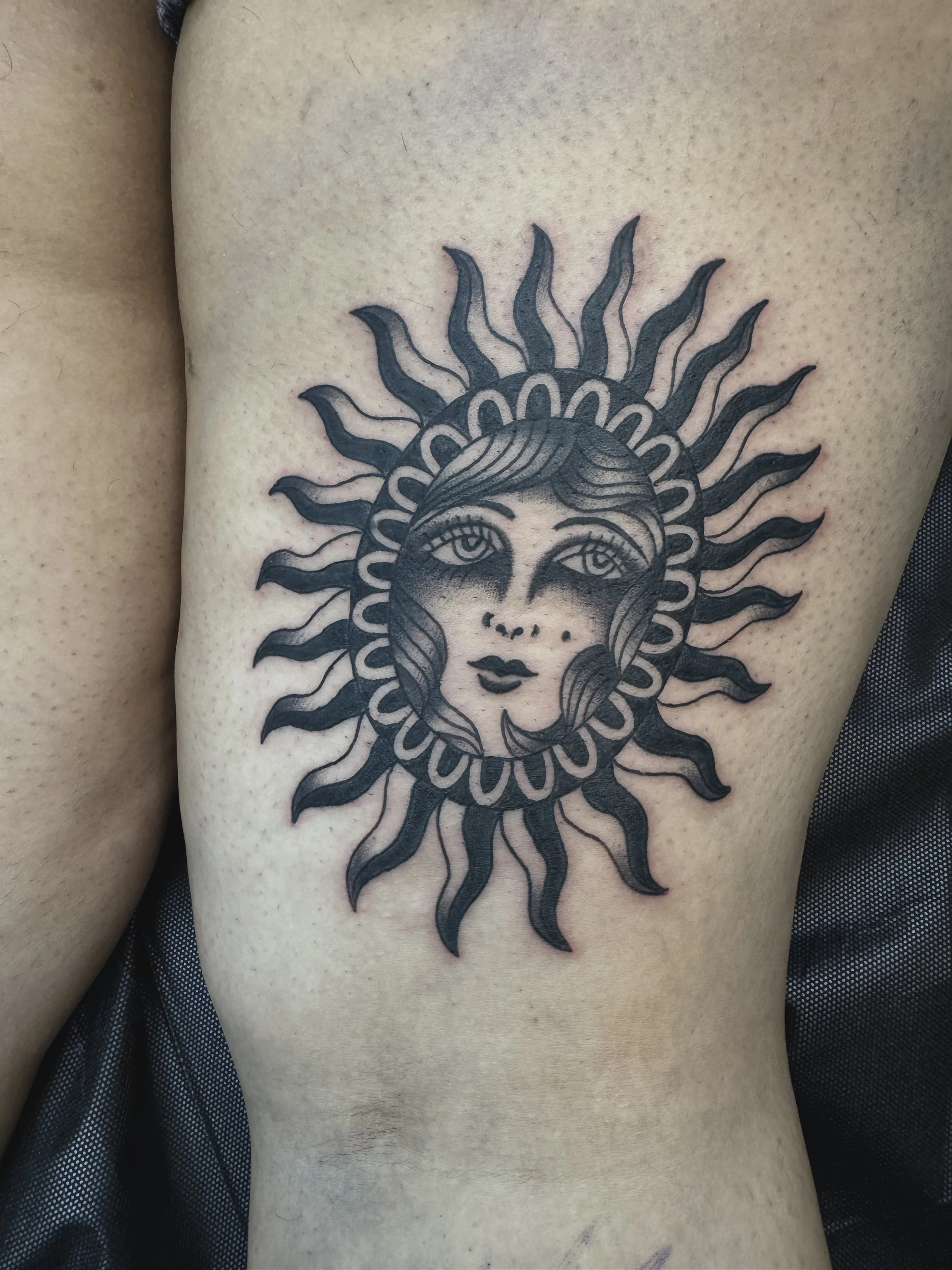 Tattoo of a woman's face with long hair, framed by a radiant sun with wavy rays.