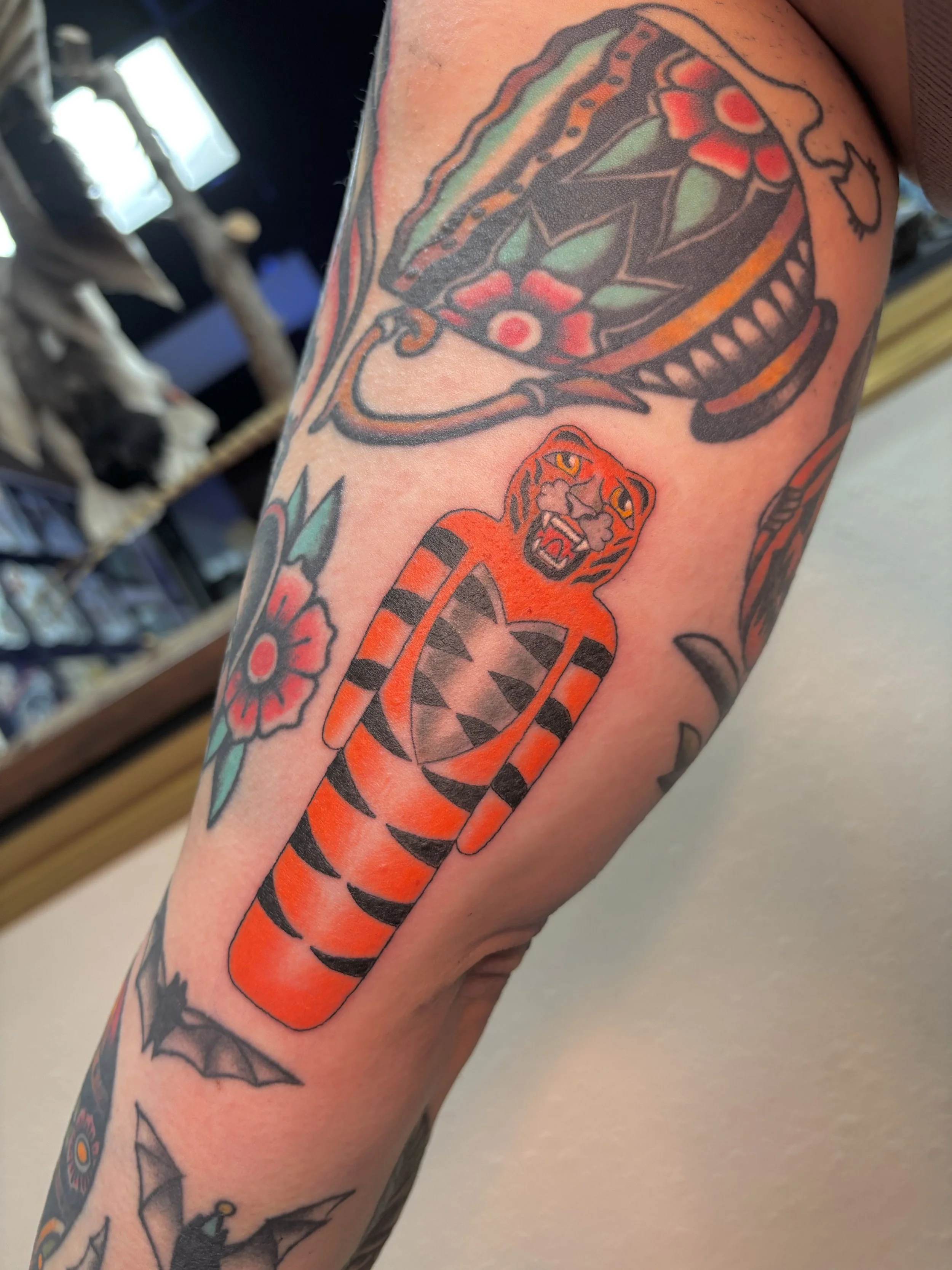 Tattoo of a tiger with orange and black stripes, surrounded by traditional tattoo designs including a snake head, a flower, a bat, and geometric patterns.