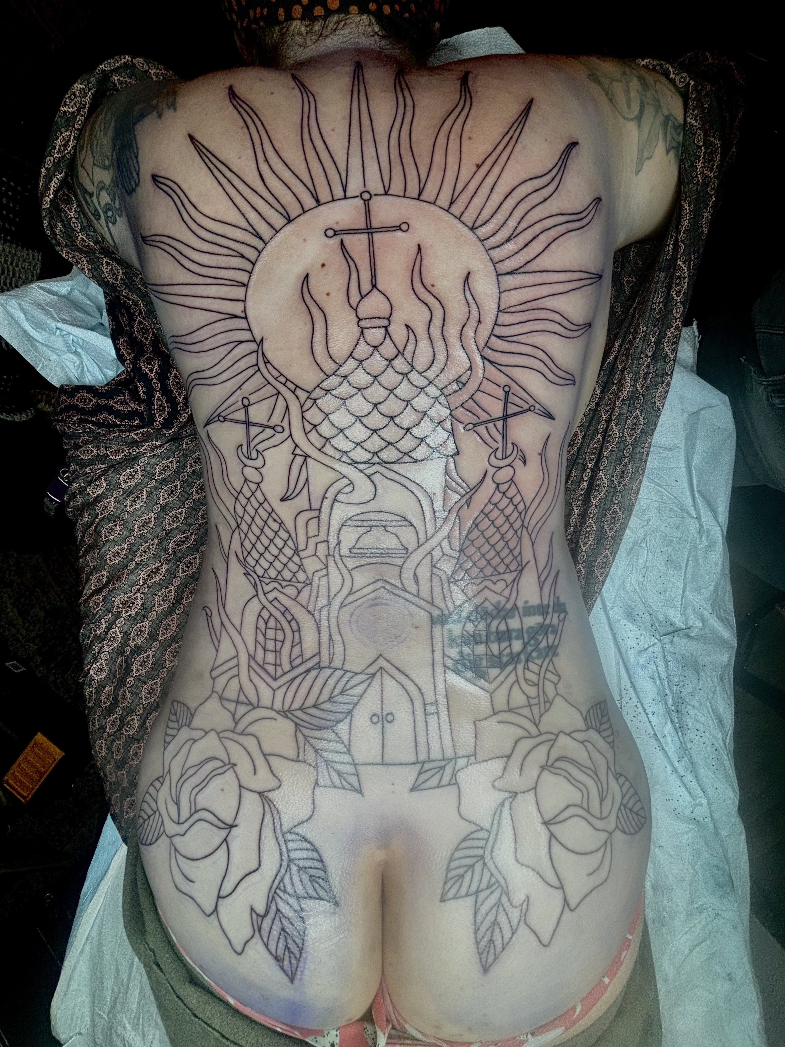 Line drawing of a tattoo on a person's back featuring a sun with radiant rays, a serpent with scales and horns, roses on the lower back, and a house with a door in the center.