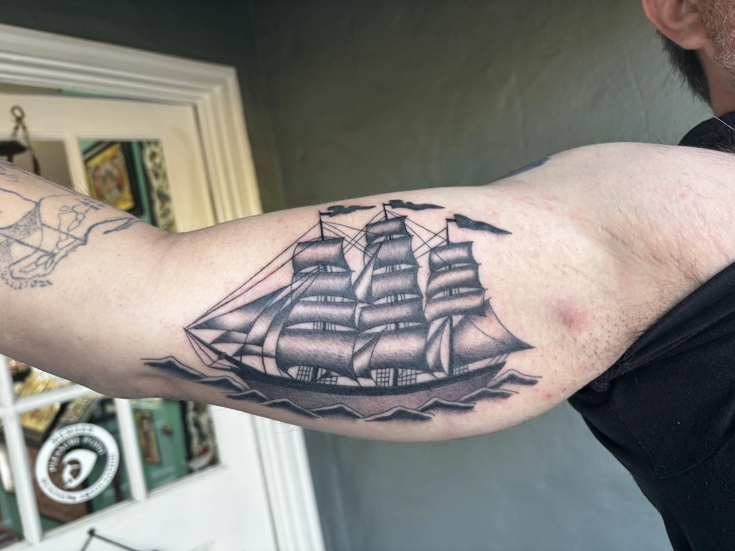 Tattoo of a vintage sailing ship with multiple sails on a person's upper arm.