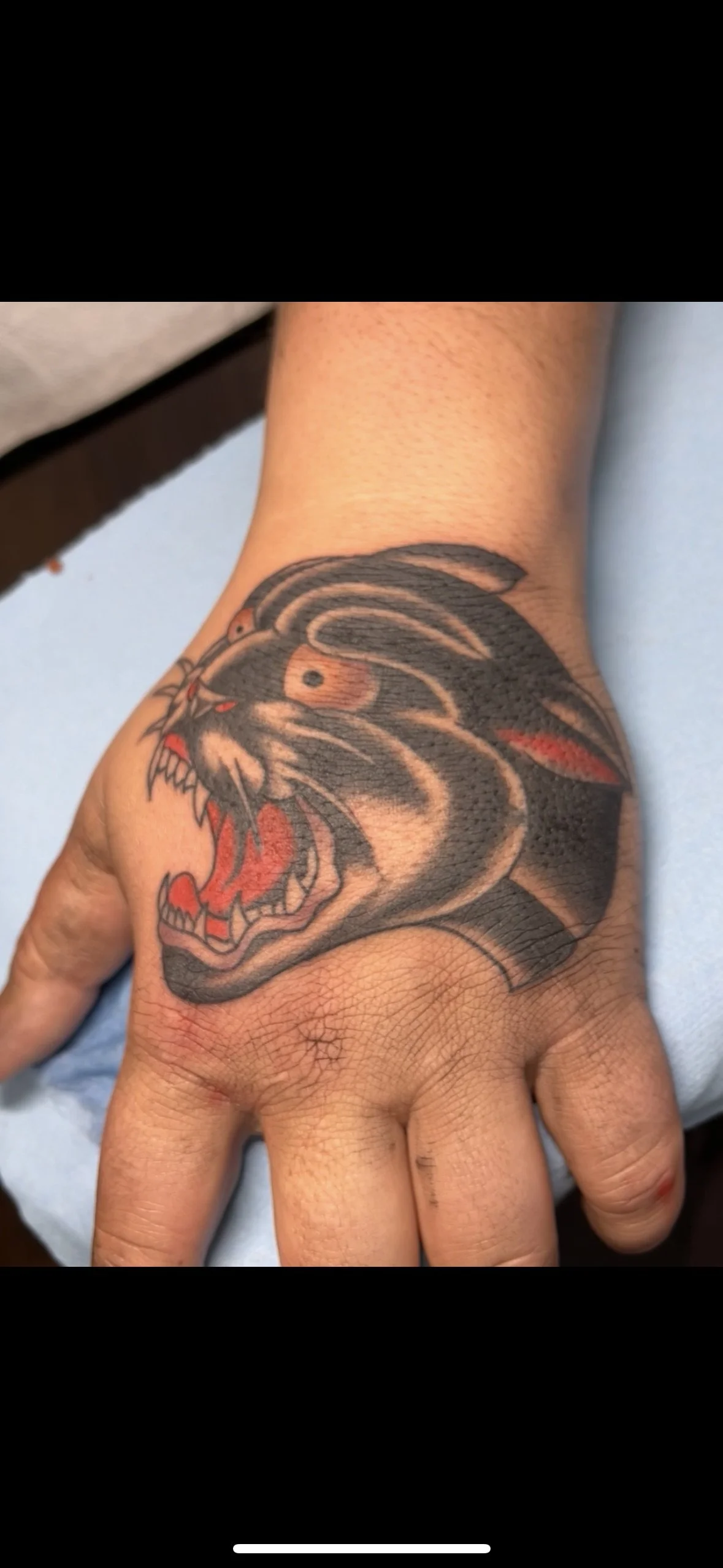 Tattoo of a roaring panther head with open mouth on a person's hand