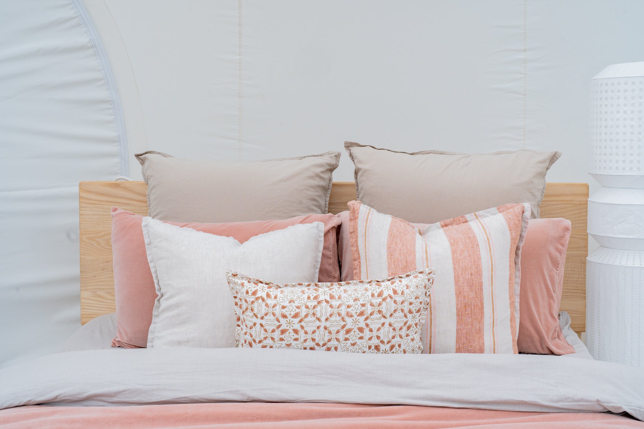 Bed with layered pillows in neutral and peach tones, patterned throw pillow, and wooden headboard.