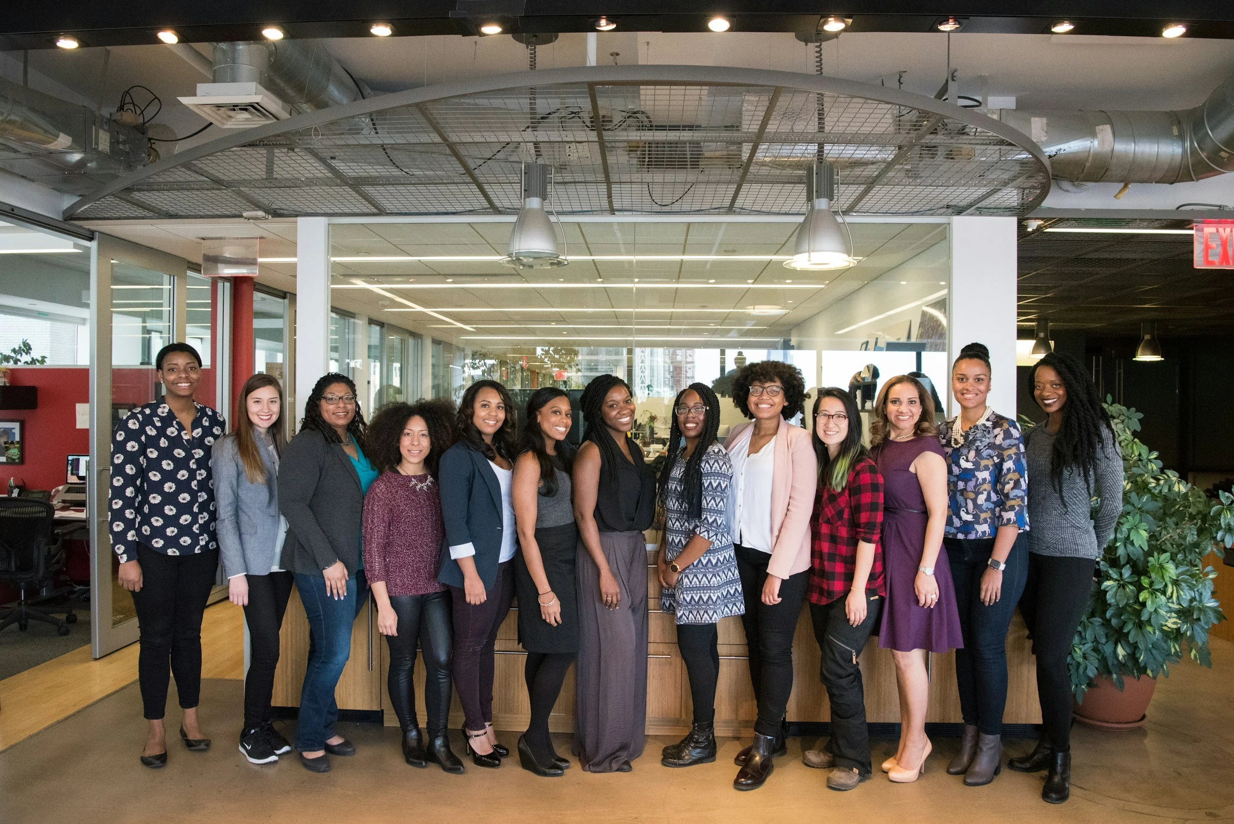Group of women standing together in an office space, smiling for the photo.