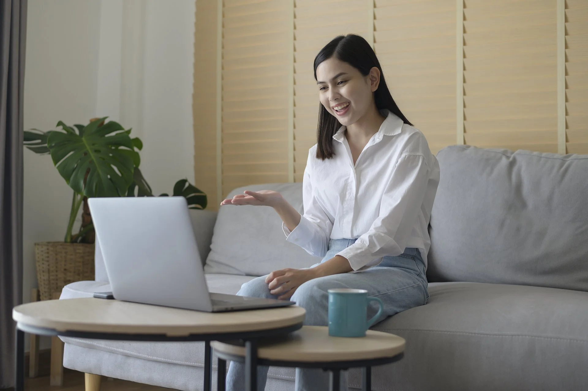 Picture of a woman engaging in an online meeting from a couch with the screen of her laptop not visible.