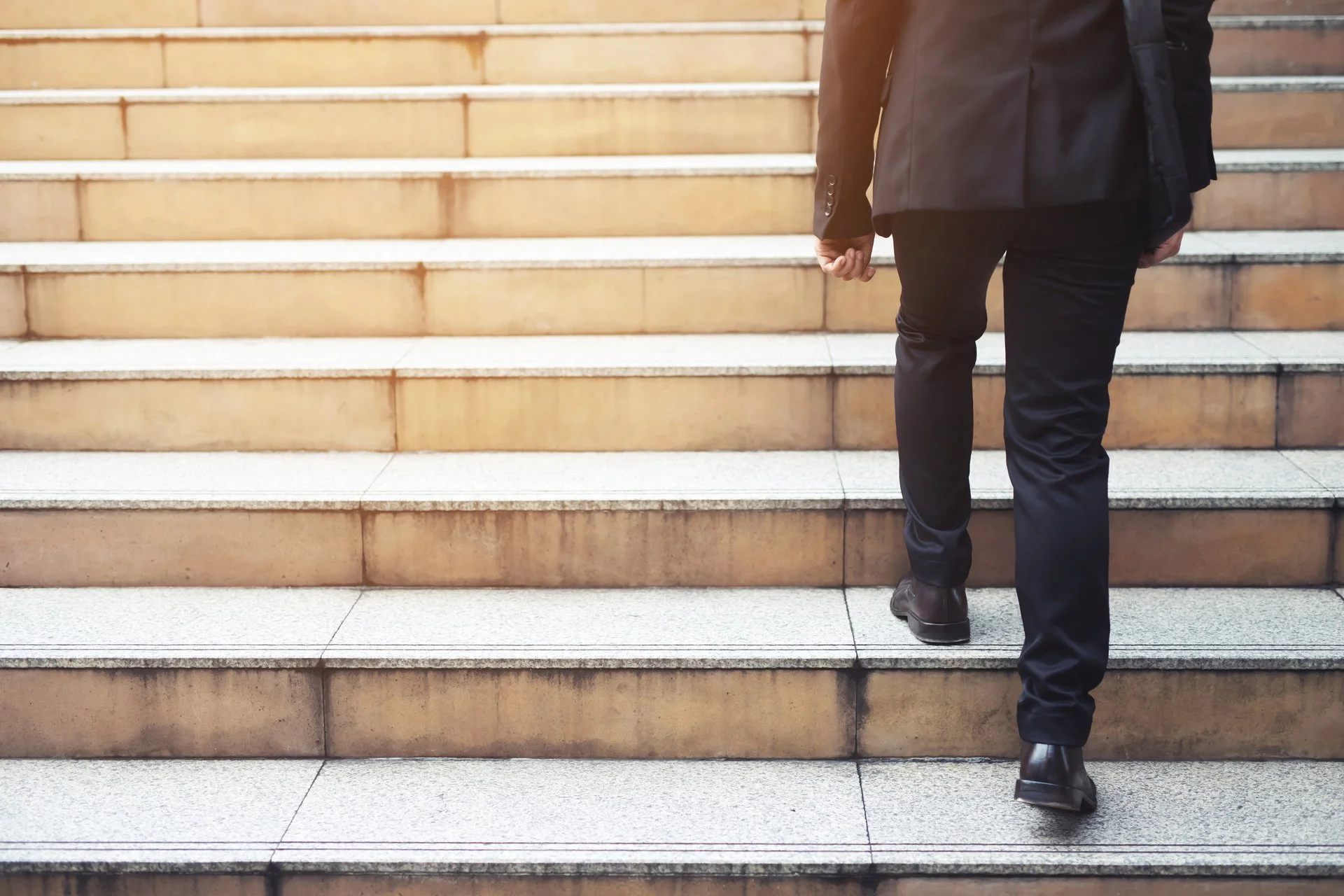 Man in a suit climbing marble steps viewed from behind.