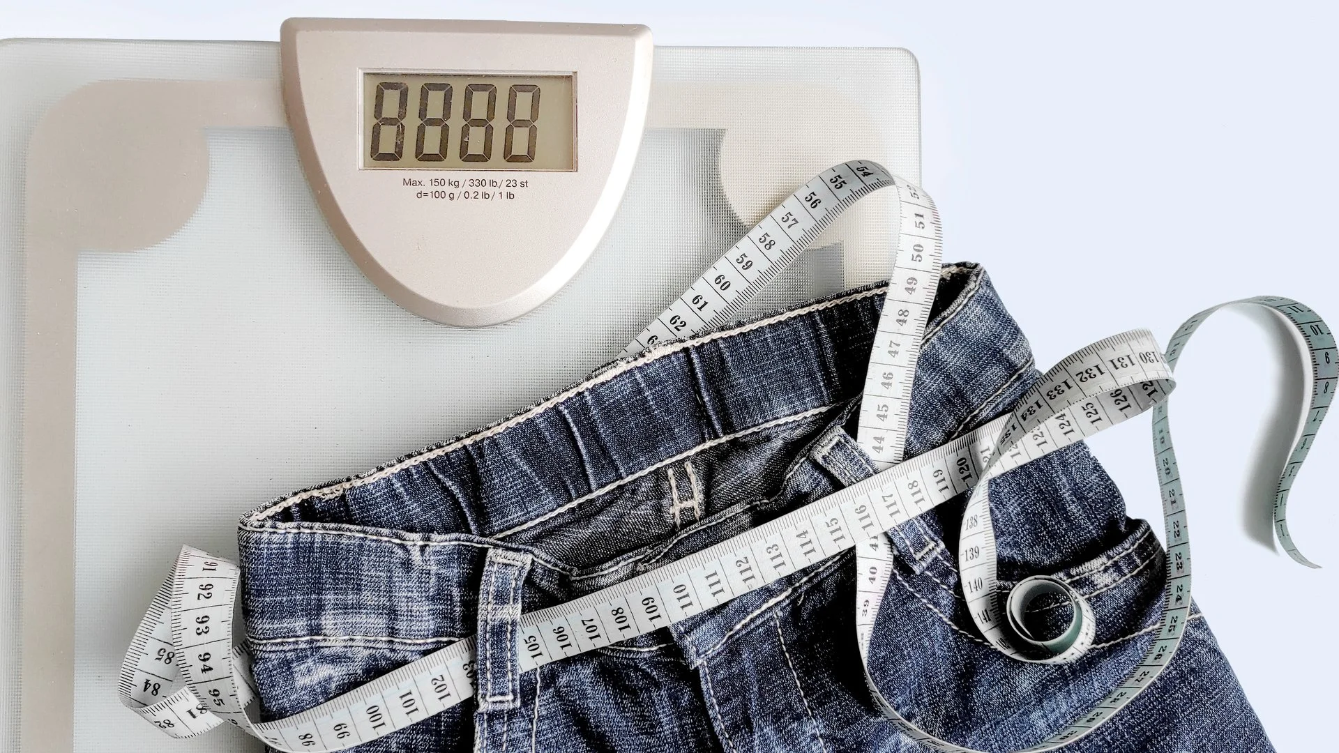 Image of a body weight scale with a measuring tape and jeans placed on top of it.