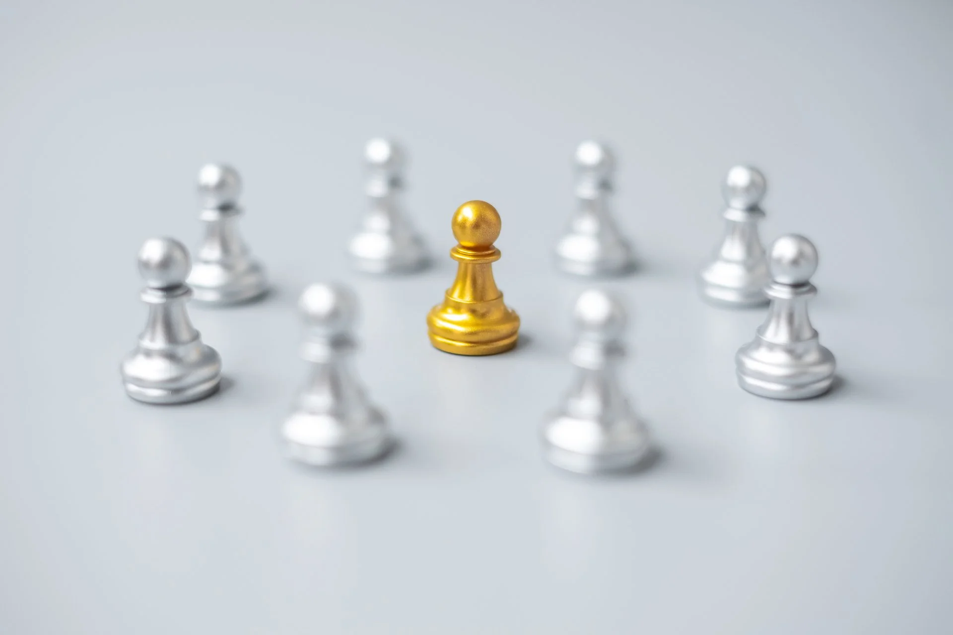 One gold chess pawn surrounded by eight silver chess pawns.