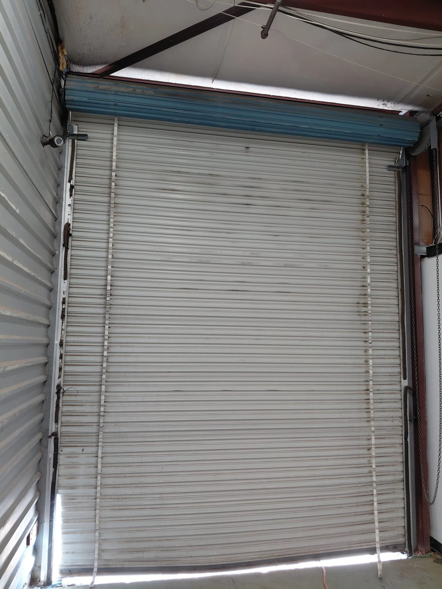Worn commercial roll-up door with blue hood before replacement