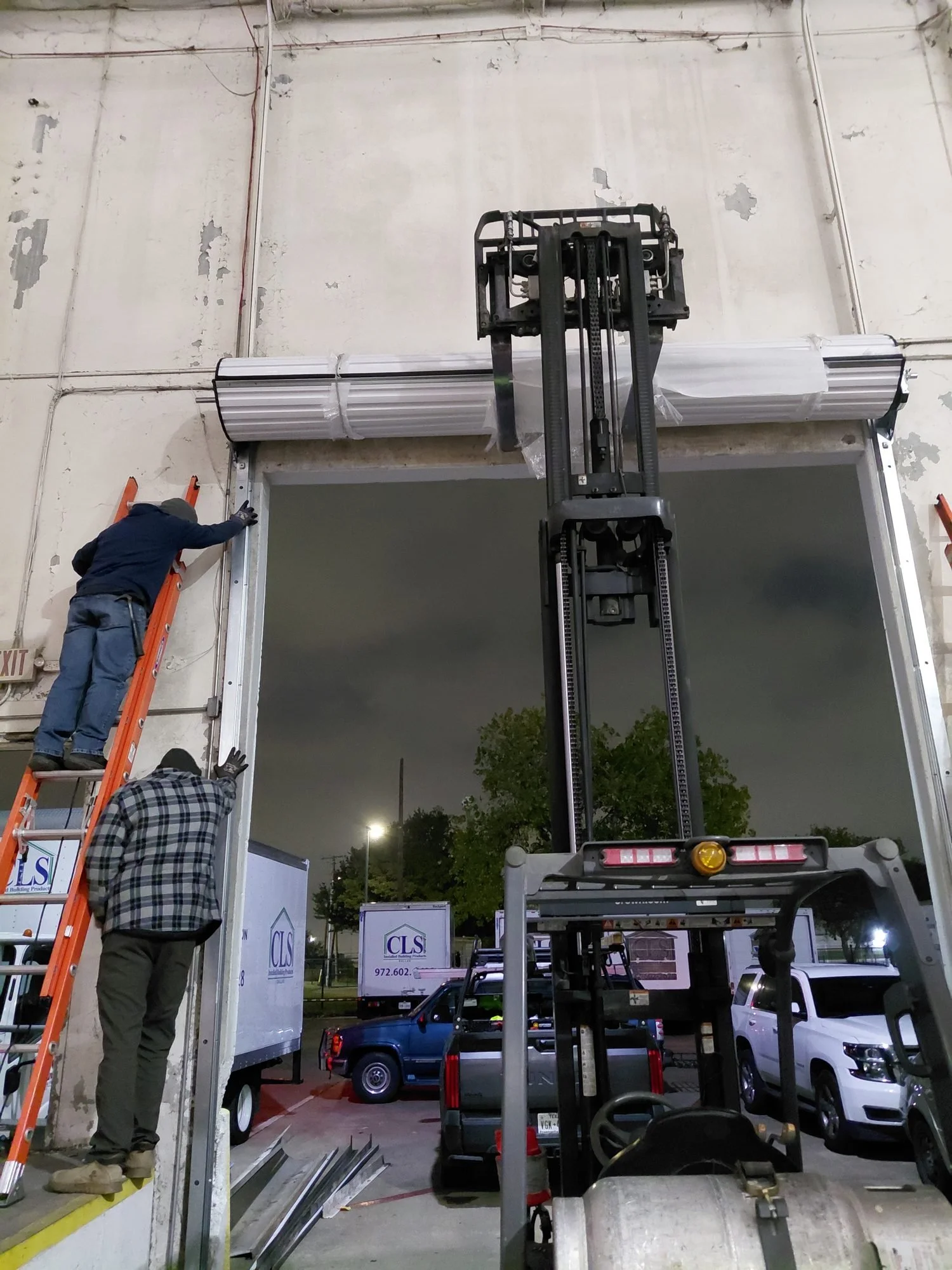 Galaxy Garage Doors crew installing a large commercial roll-up door at night with a lift in Arlington, TX