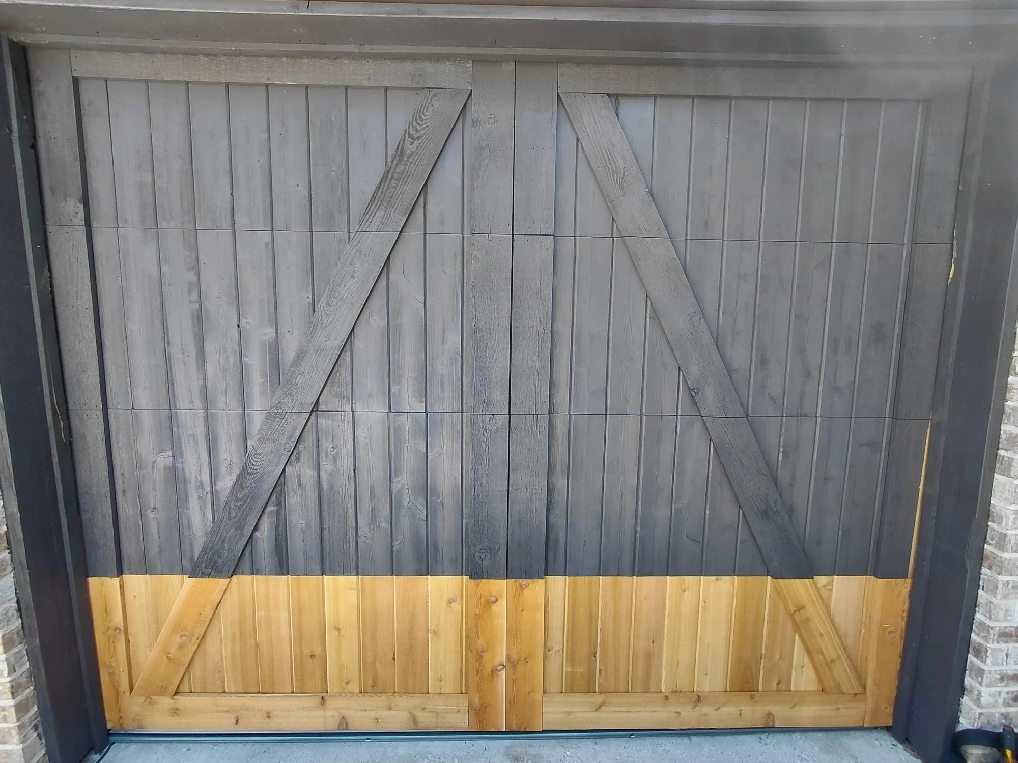 Wood barn-style garage door after repair with new cedar lower panels