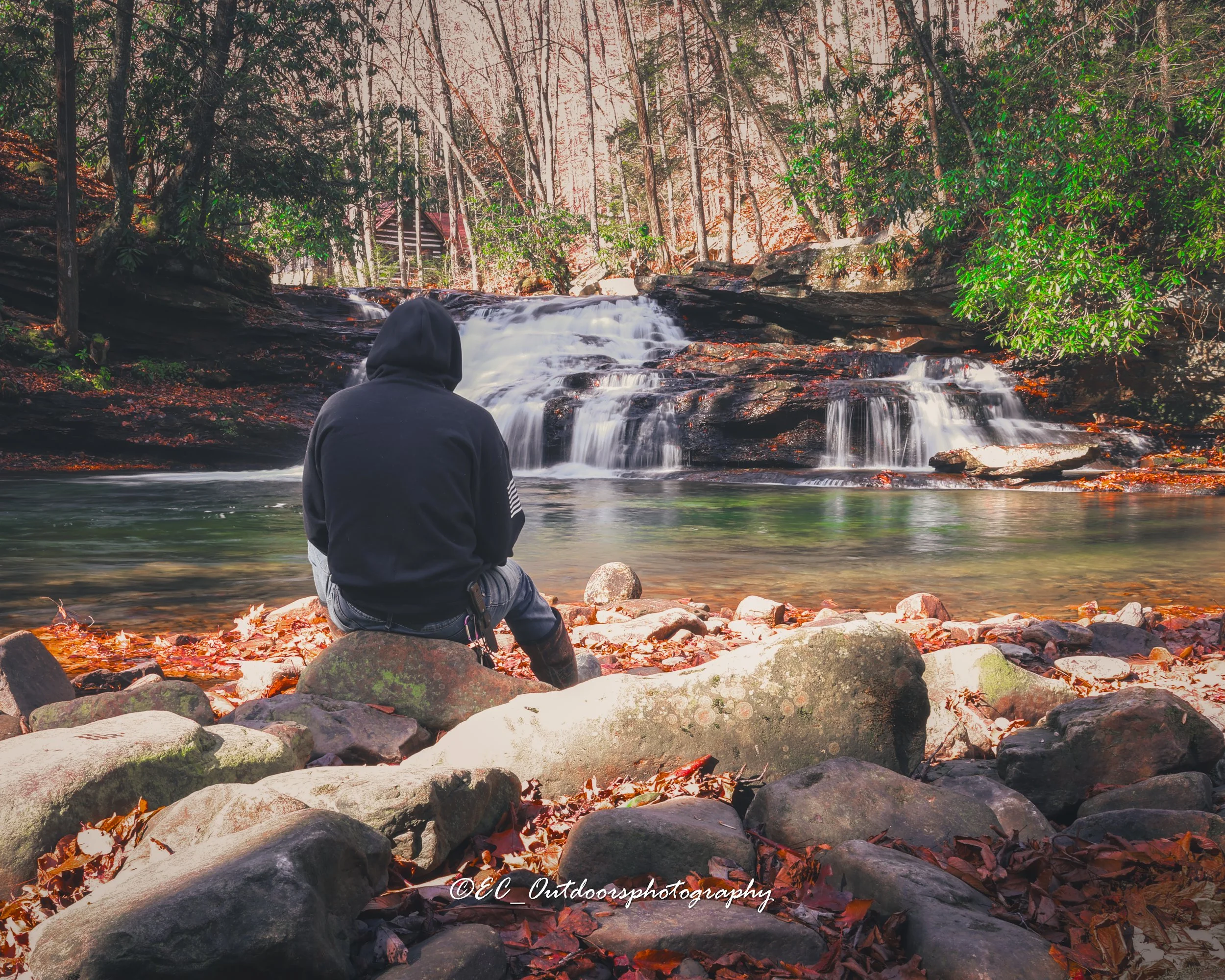 Person sitting on rocks by a waterfall in a forest.