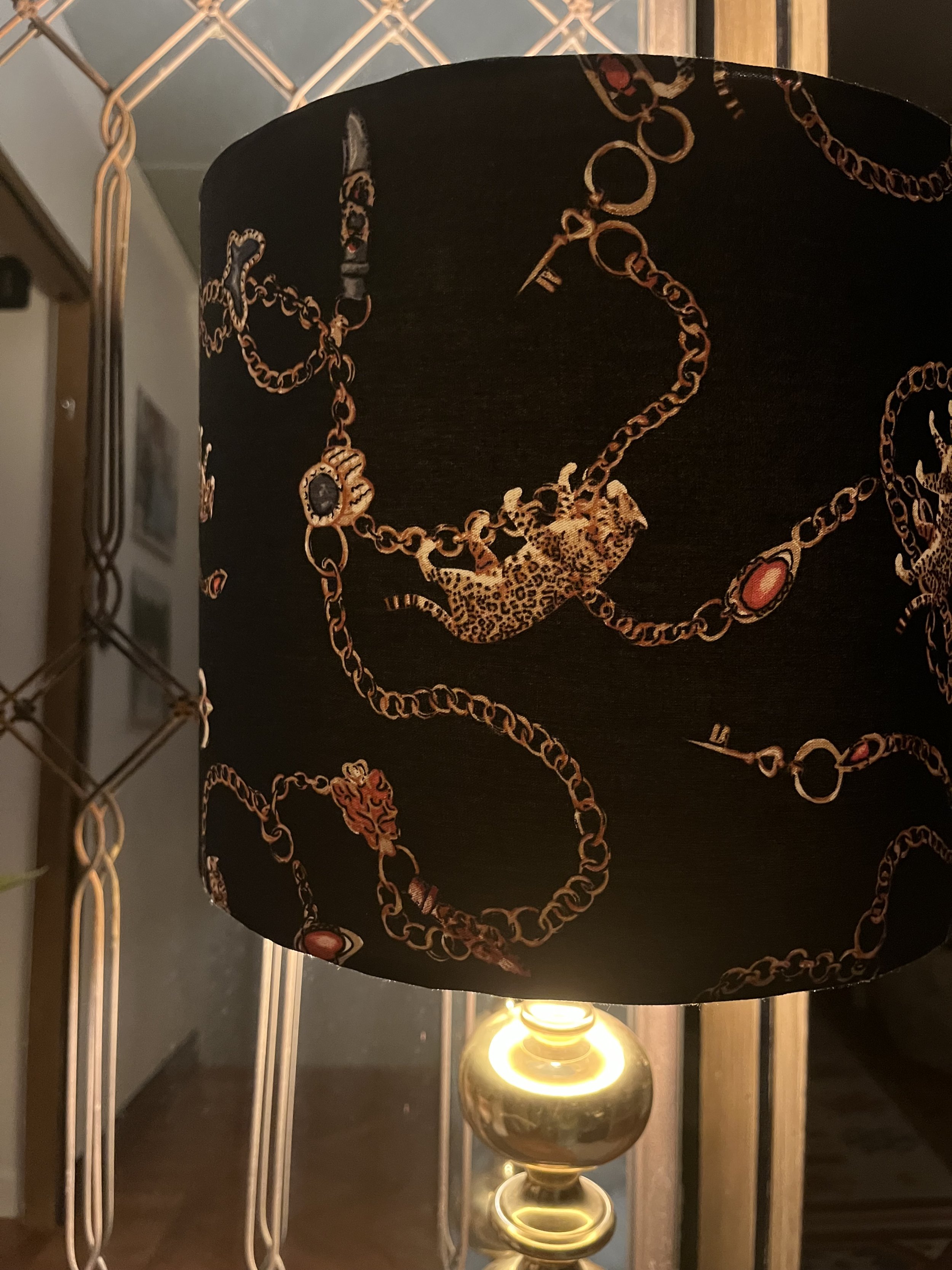 Decorative lamp with a patterned black lampshade featuring chains and leopard design, placed in front of a mirrored wall.