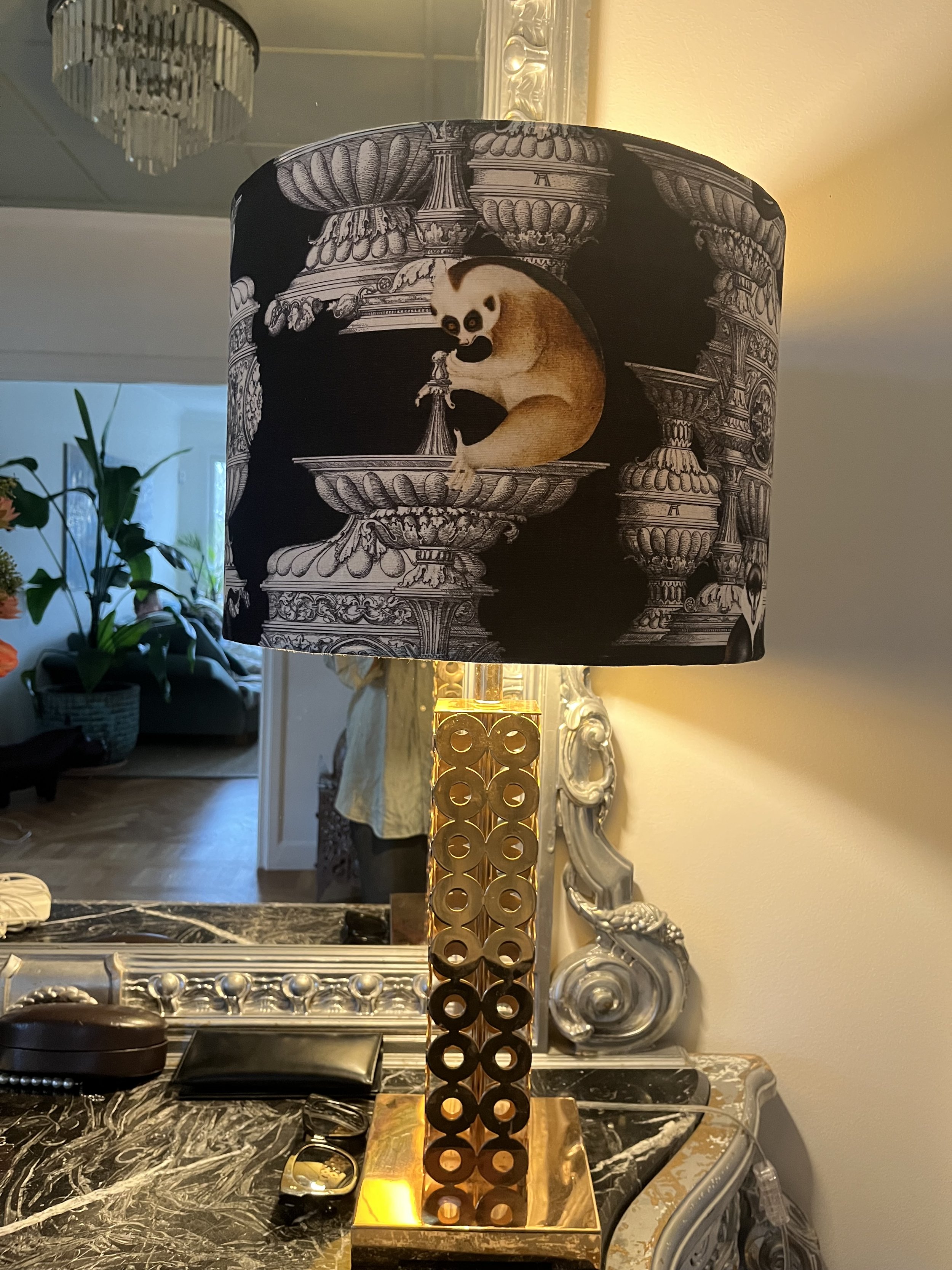 Decorative table lamp with ornate shade featuring a vintage-style animal print, placed on a marble-topped surface with a mirror in the background.