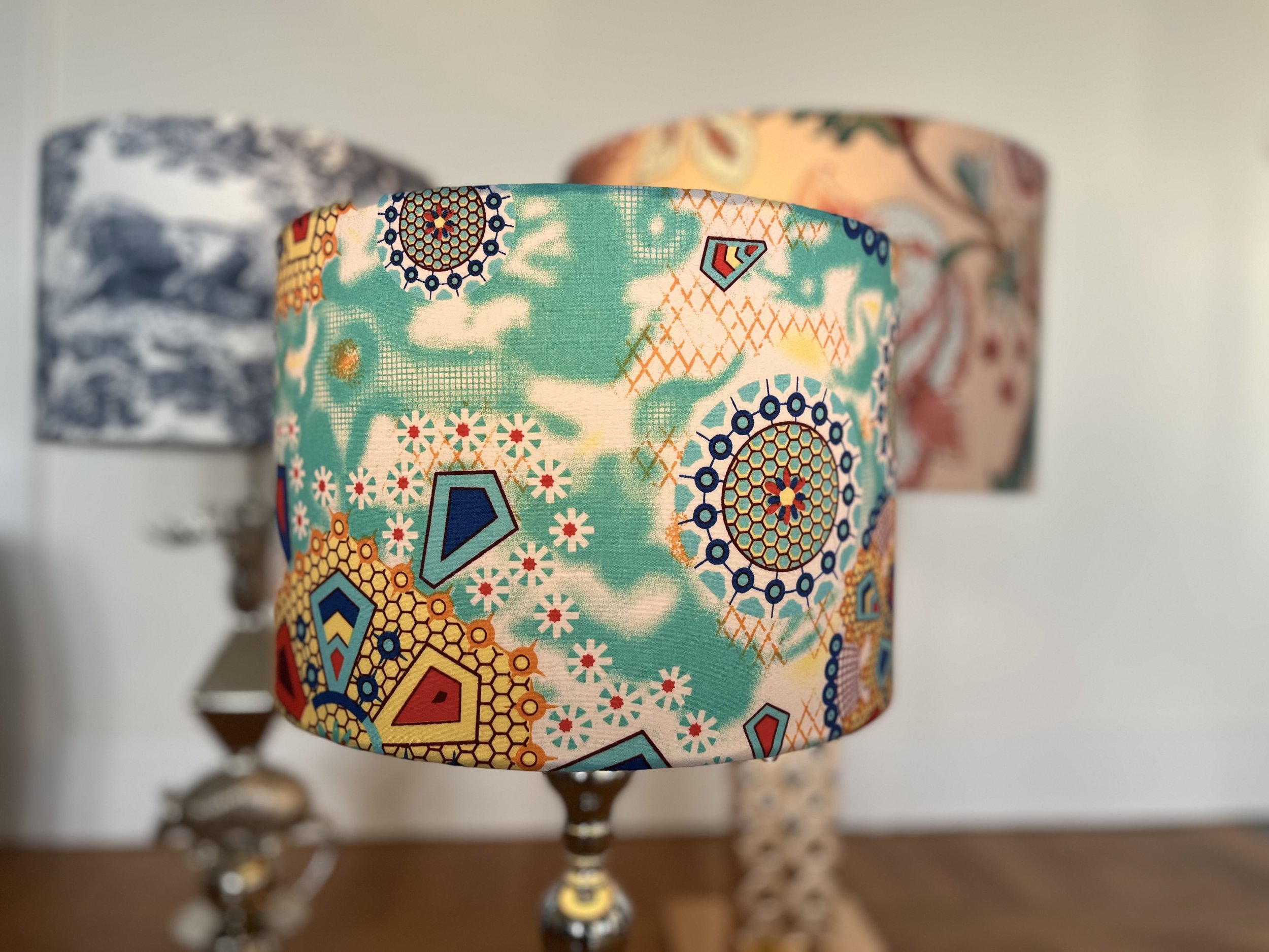 Colorful lampshade with geometric and floral patterns next to two other patterned lampshades, one in blue and white.