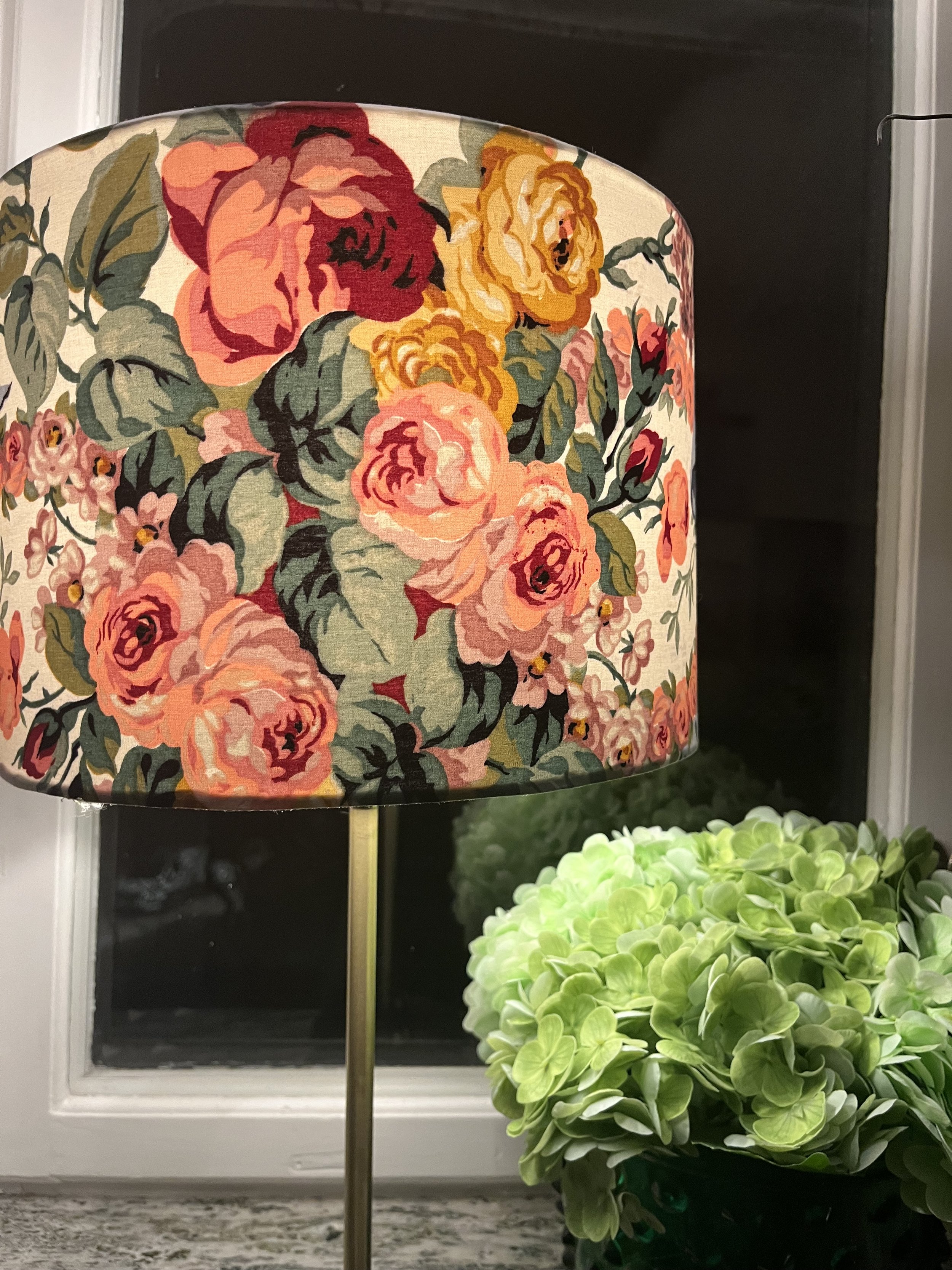 Floral-patterned lampshade next to a green hydrangea bouquet on a windowsill.