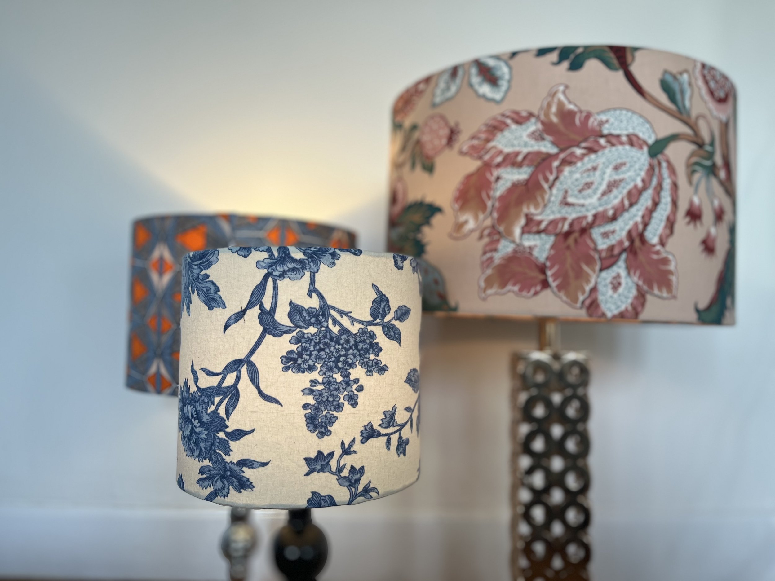 Three decorative lamp shades with floral and geometric patterns; front lamp features a blue floral design on a white background.