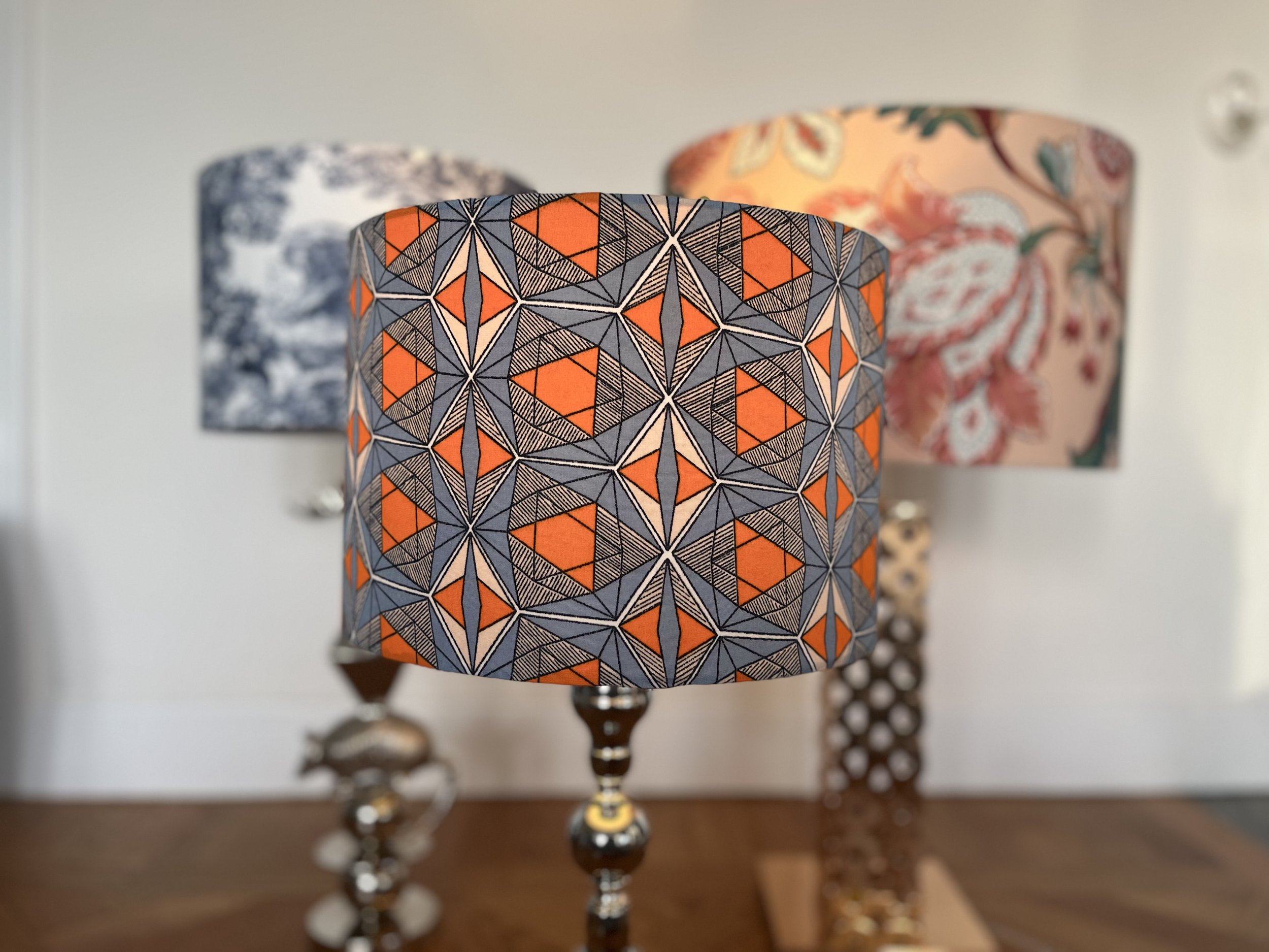 Three decorative lampshades displayed in a row, featuring geometric, floral, and abstract patterns.