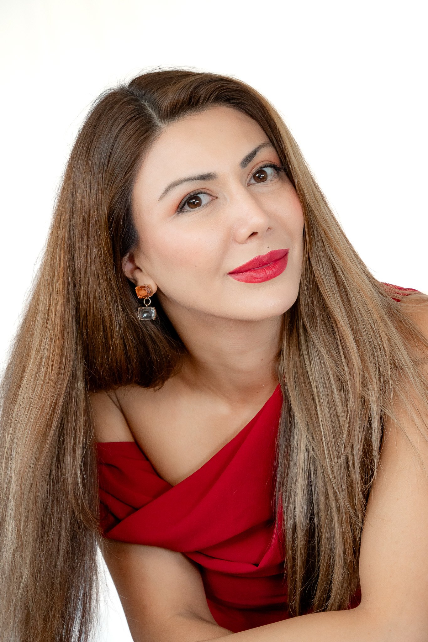 Porträt einer Frau mit langem braunem Haar und rotem Lippenstift, die ein rotes Kleid trägt.