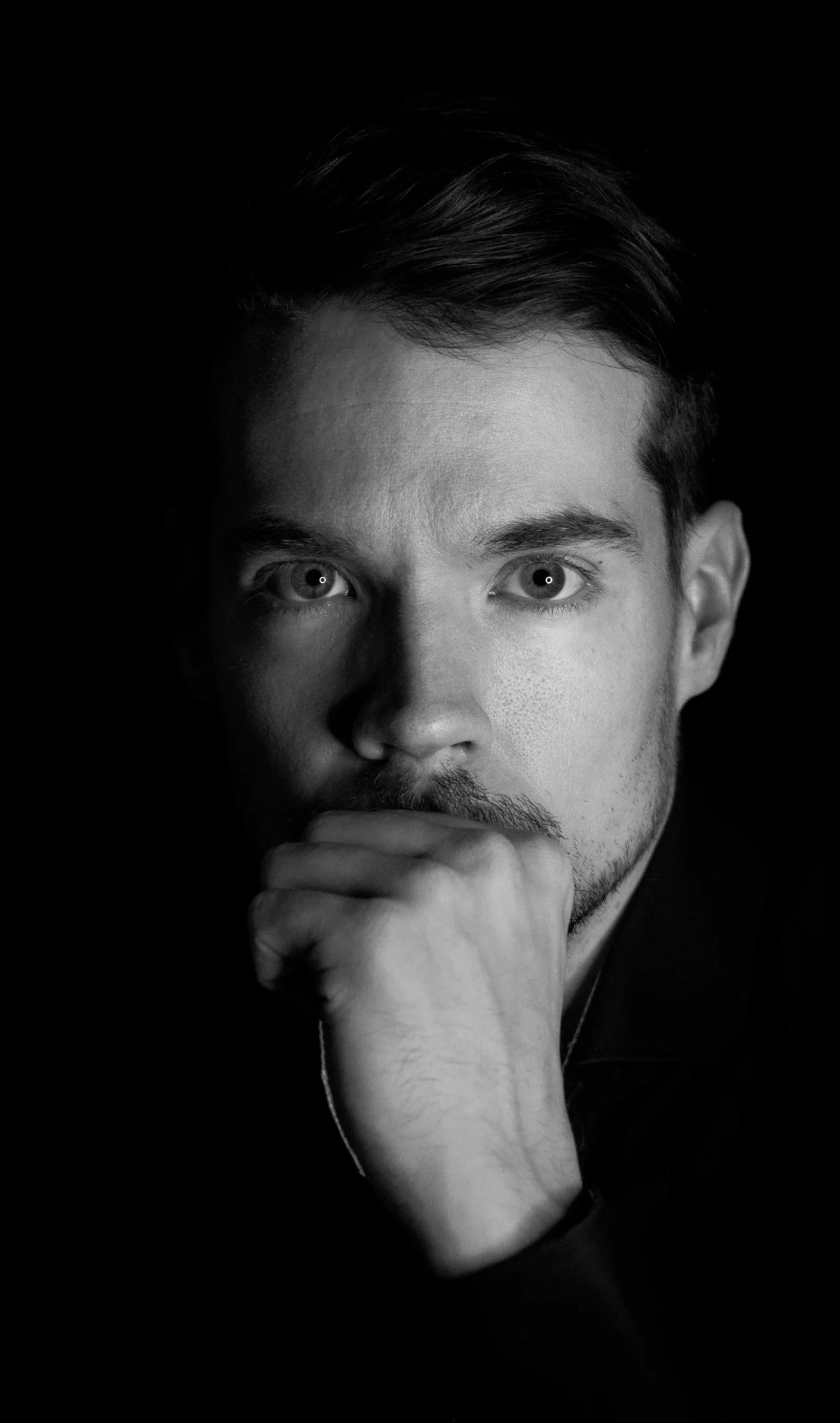 Porträt eines nachdenklichen Mannes im Schwarz-Weiß-Foto, der mit der Faust am Kinn schaut.