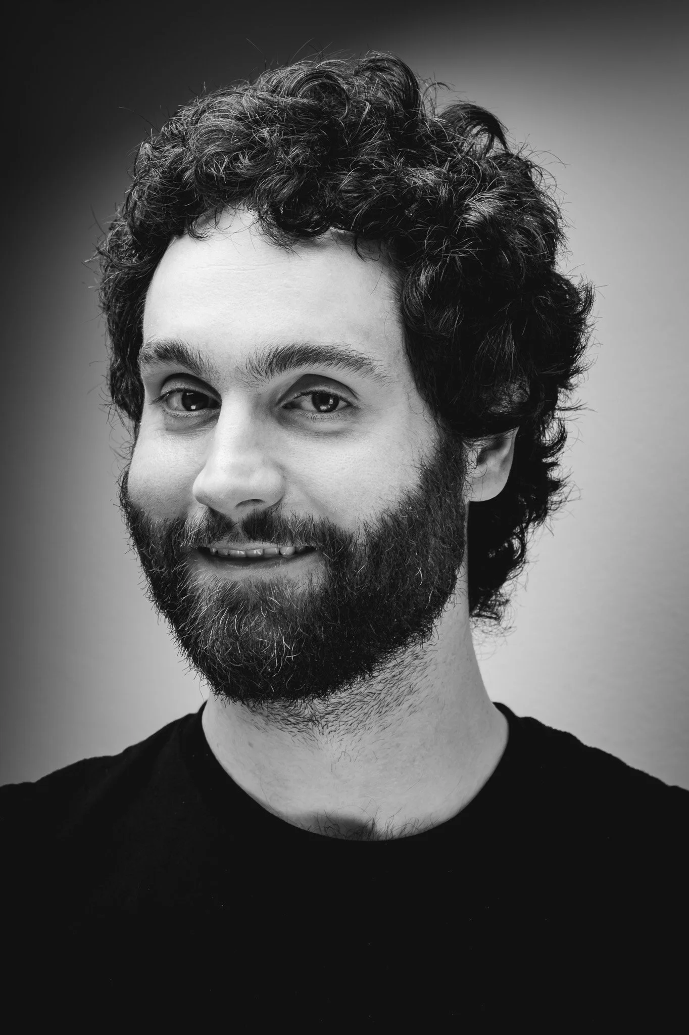 Schwarz-weiß Porträt eines lächelnden Mannes mit lockigem Haar und Vollbart.