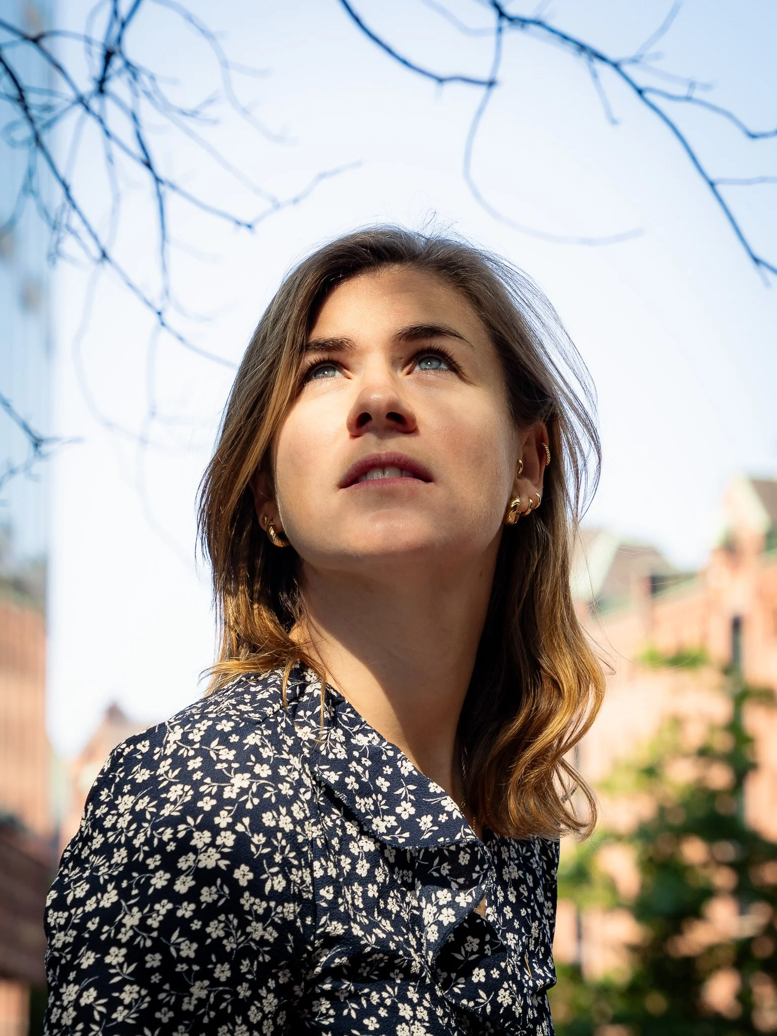 Eine Frau schaut nach oben in einem städtischen Umfeld mit Ästen im Hintergrund.