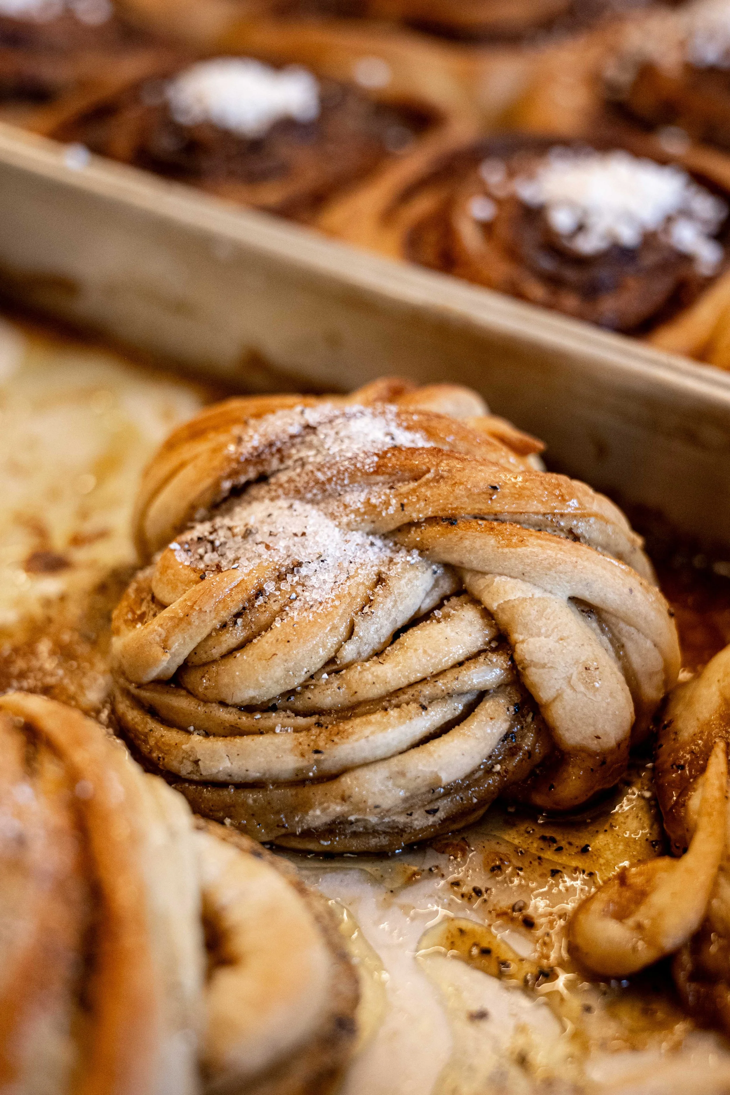 Tæt på en kringle med sukker på toppen, omgivet af flere kringles, med smør, kanel og sukker.