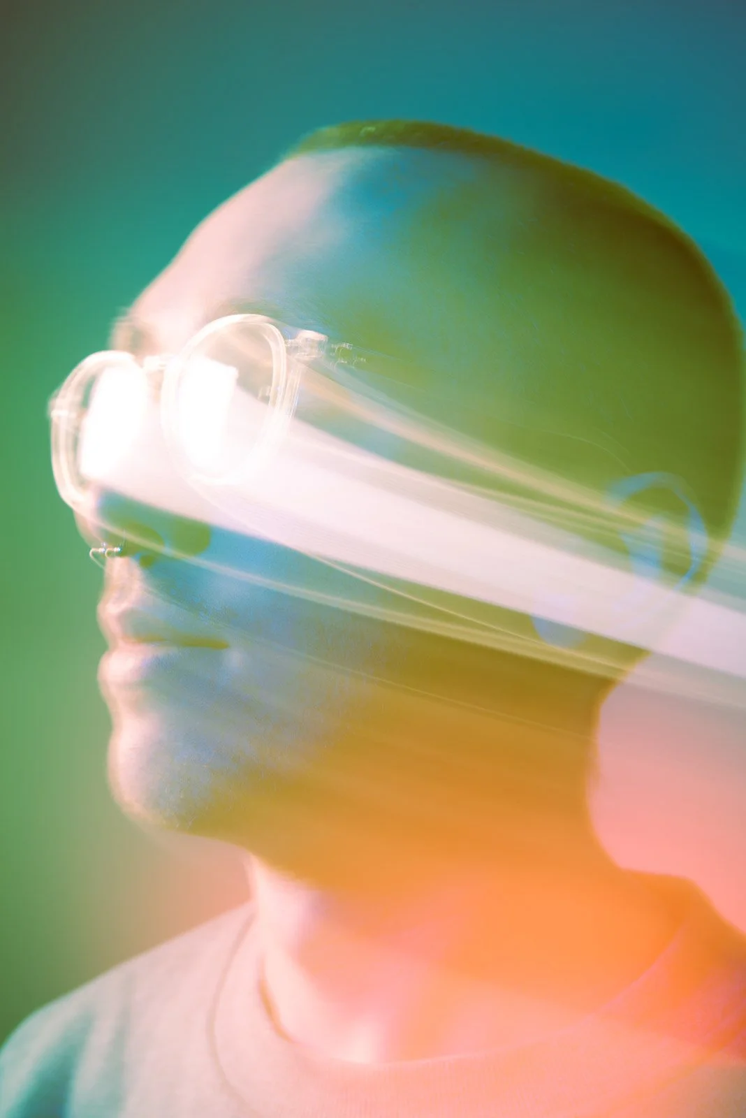 Side profile of a person with short hair wearing glasses, with colorful light streaks across the image.