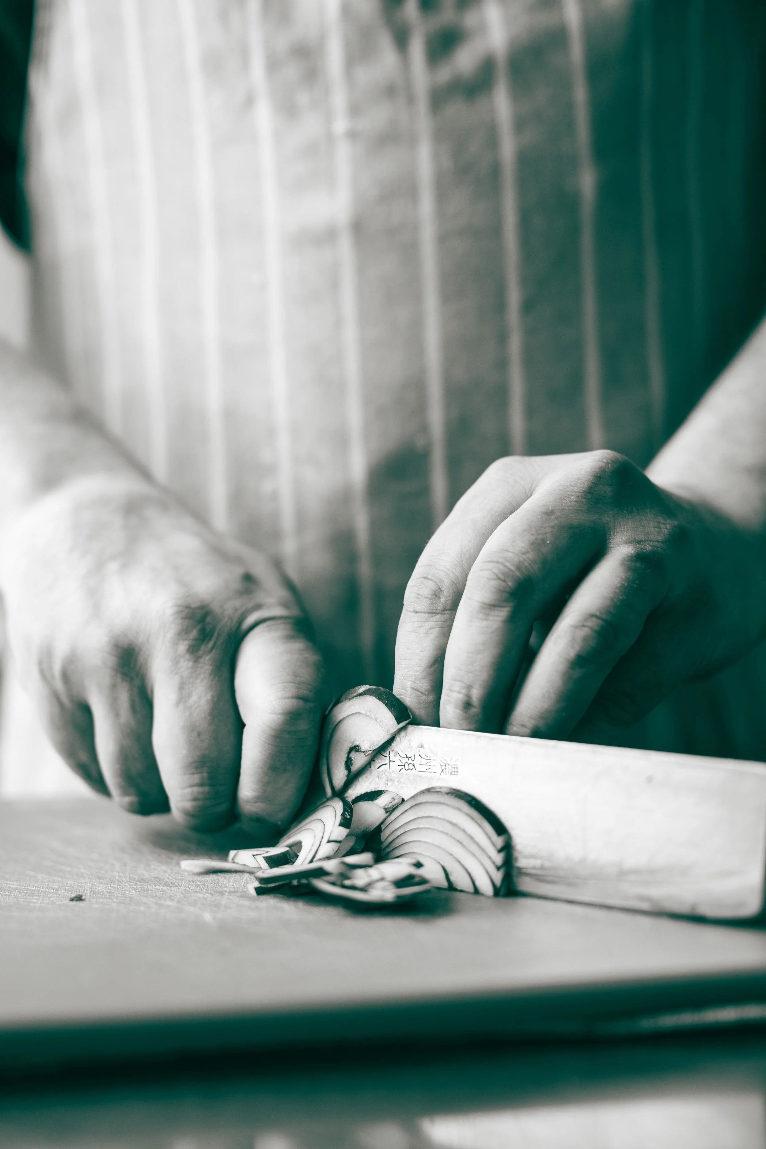 Close-up of a person's hand using a tool to carve or inscribe characters on a piece of material, with tatami flooring in the background.