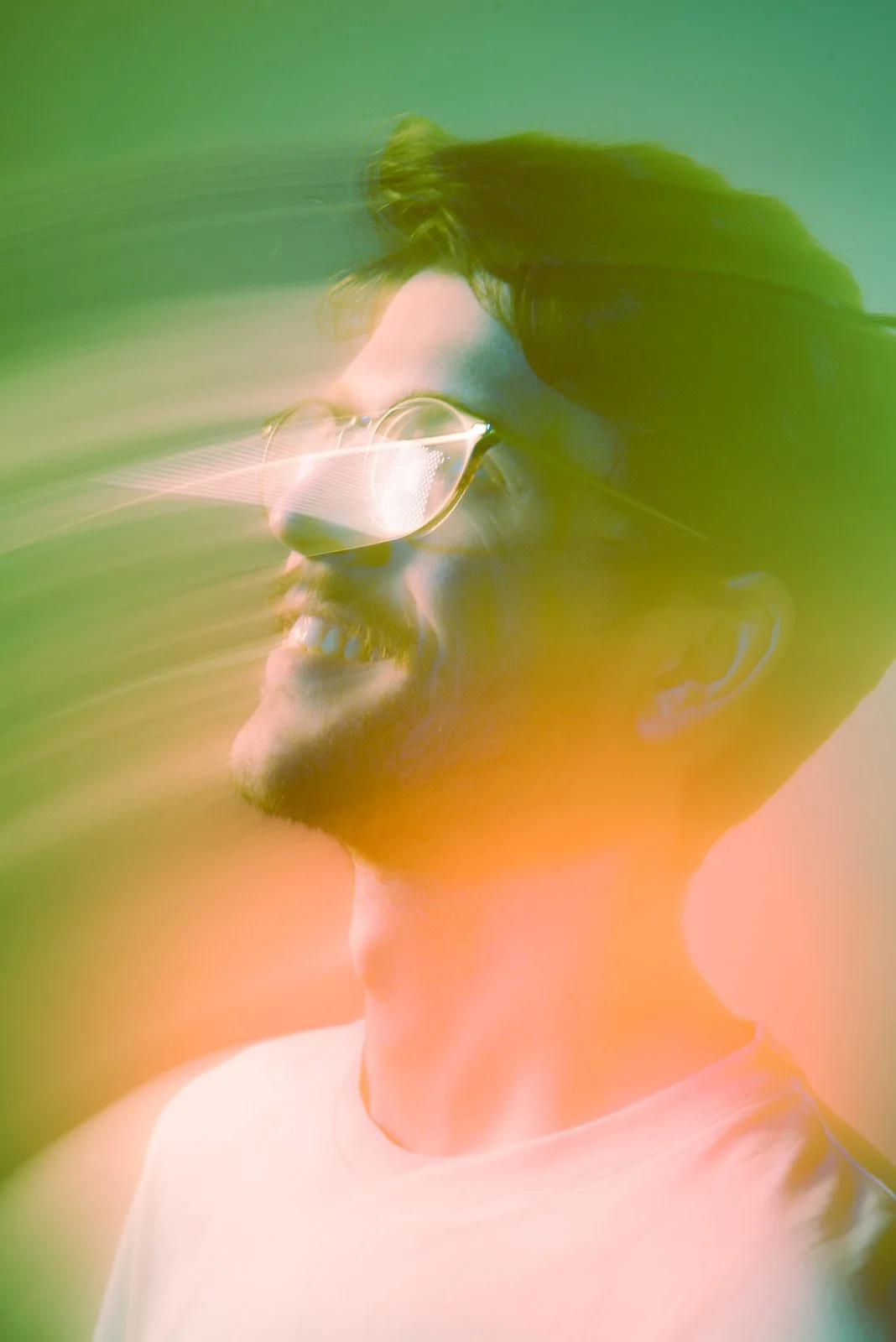 A young man with dark hair and glasses smiling, with colorful light effects.