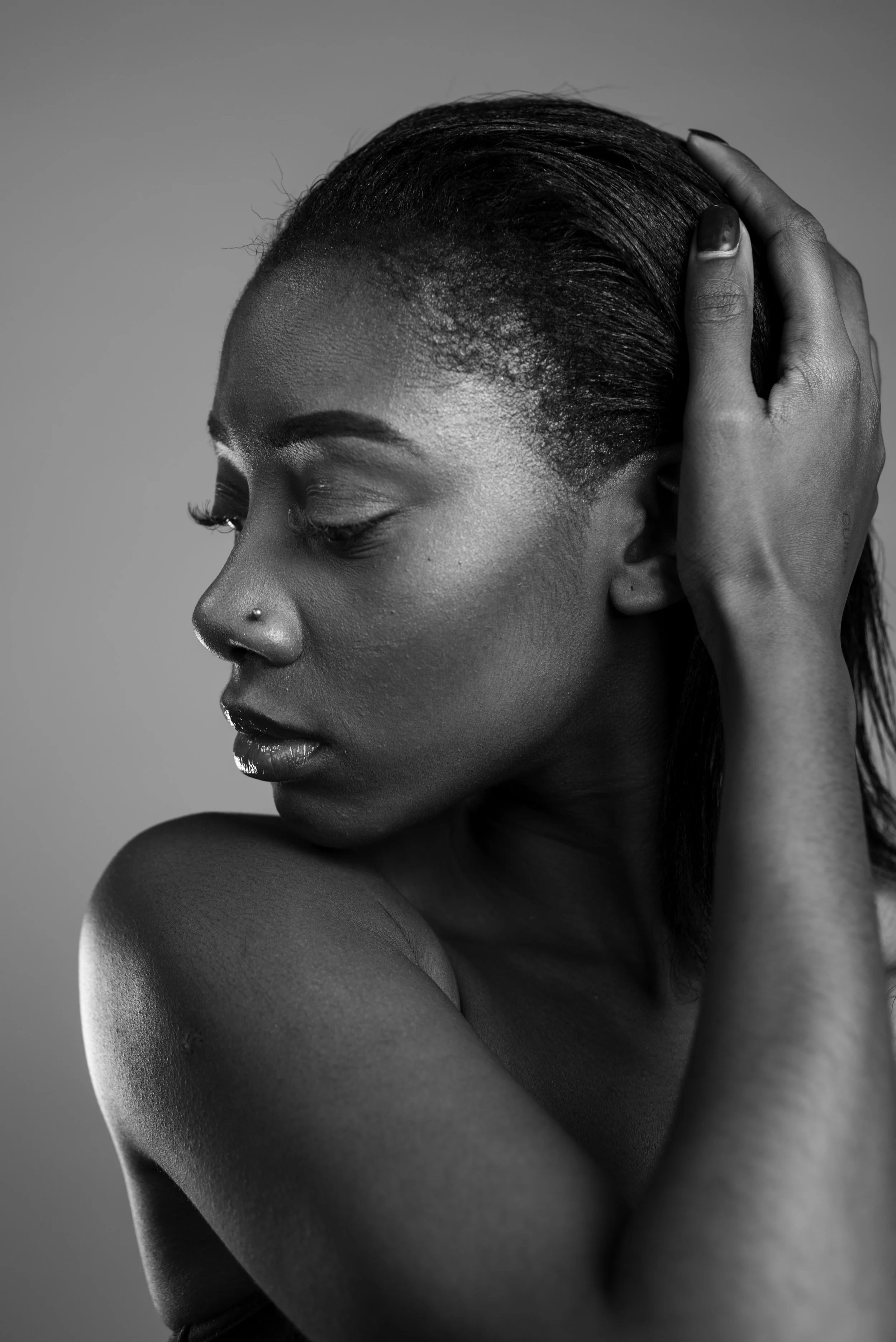 Black and white photo of a woman with closed eyes, head resting on her hand, showing her nose piercing and smooth skin.