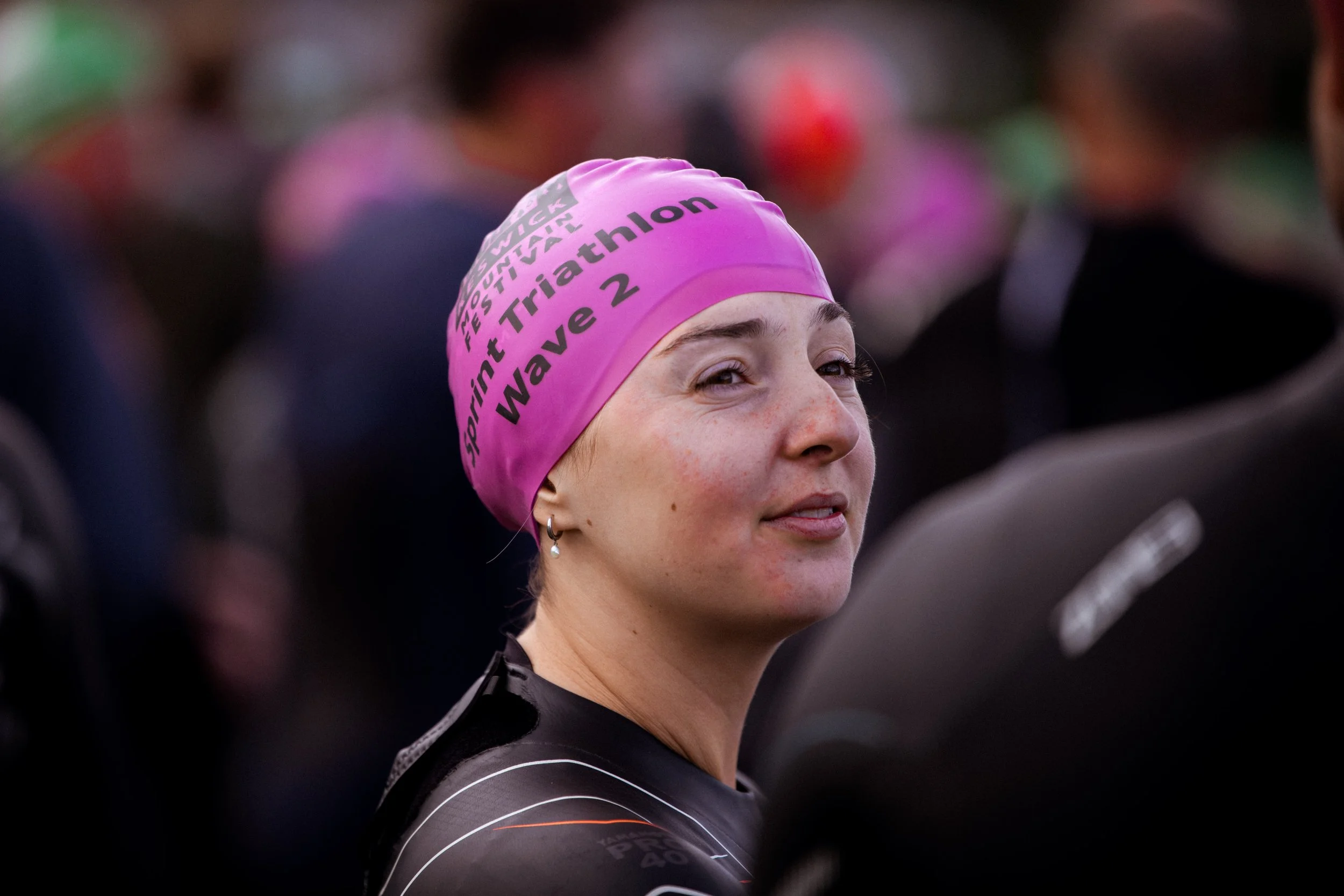 A female athlete wearing a pink swim cap with text that says 'California International Triathlon WAVE 2' and a black athletic outfit, at a triathlon event.