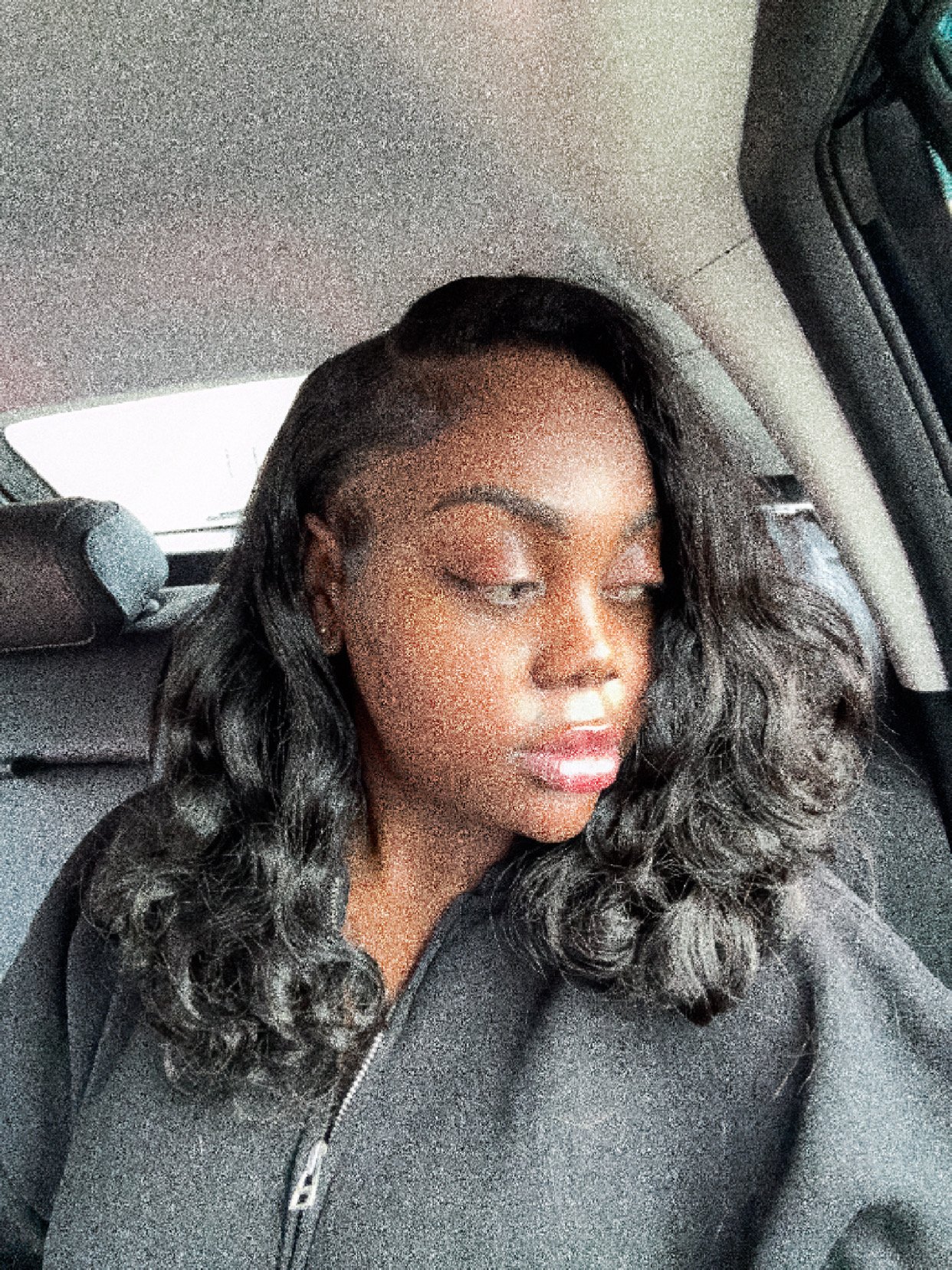 Femme aux cheveux ondulés, assise dans une voiture, portant un pull noir.