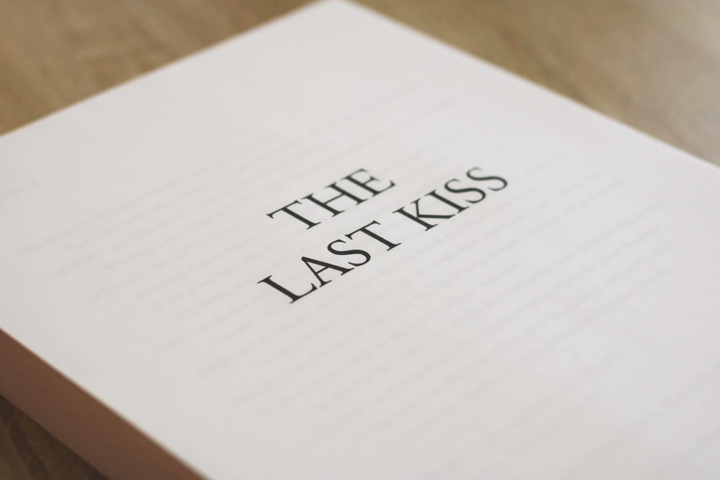 Close-up of a white paper with black text that reads, "THE LAST KISS," placed on a wooden surface.