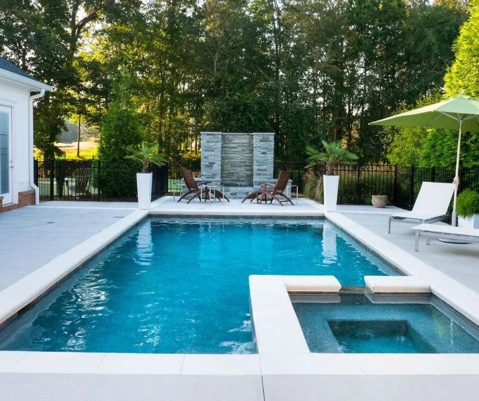 Backyard pool in Gilbert AZ with lounge chairs, umbrella, stone water feature, and black fence—professionally maintained by local pool cleaning service