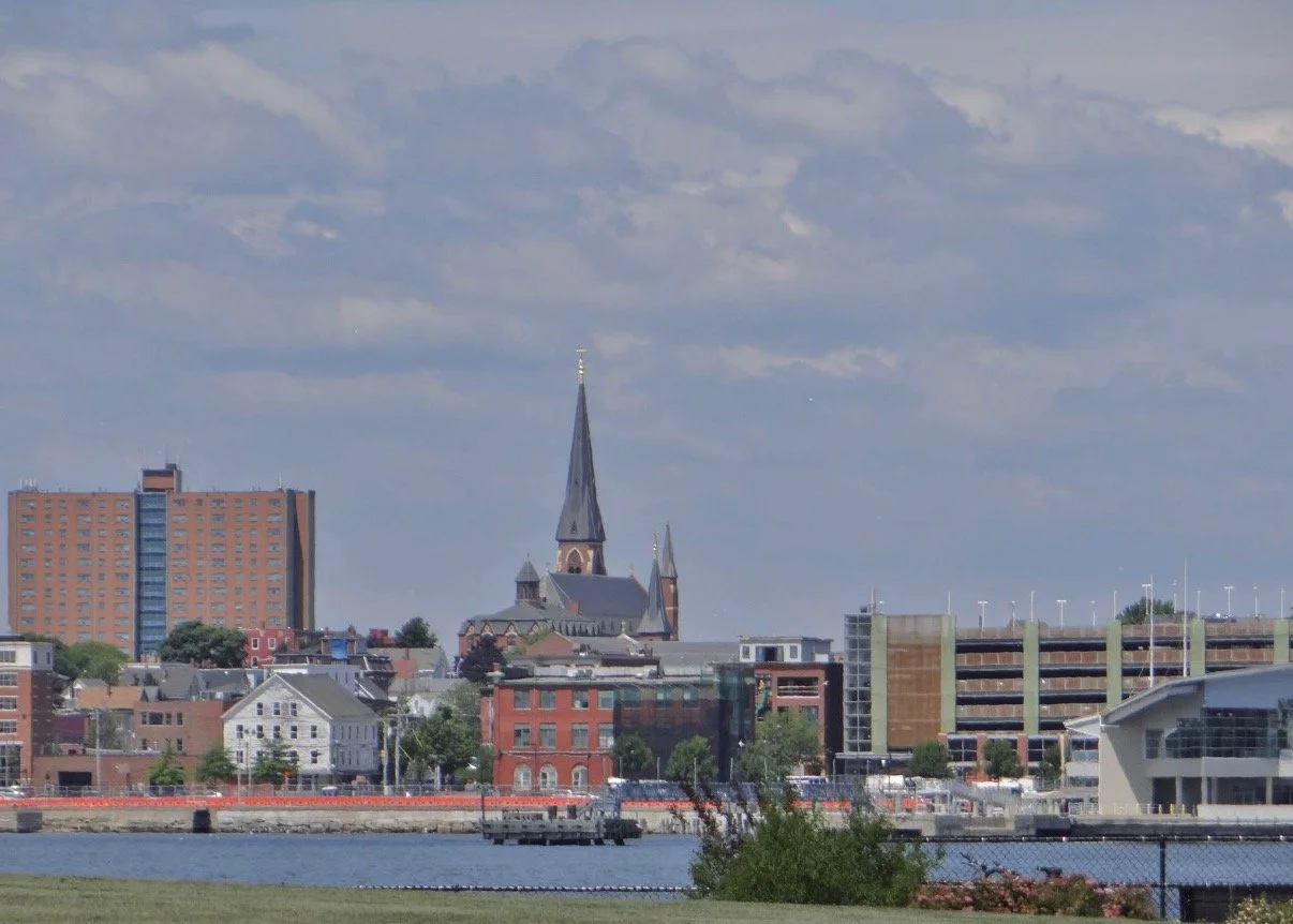 City waterfront with a church spire and brick buildings.