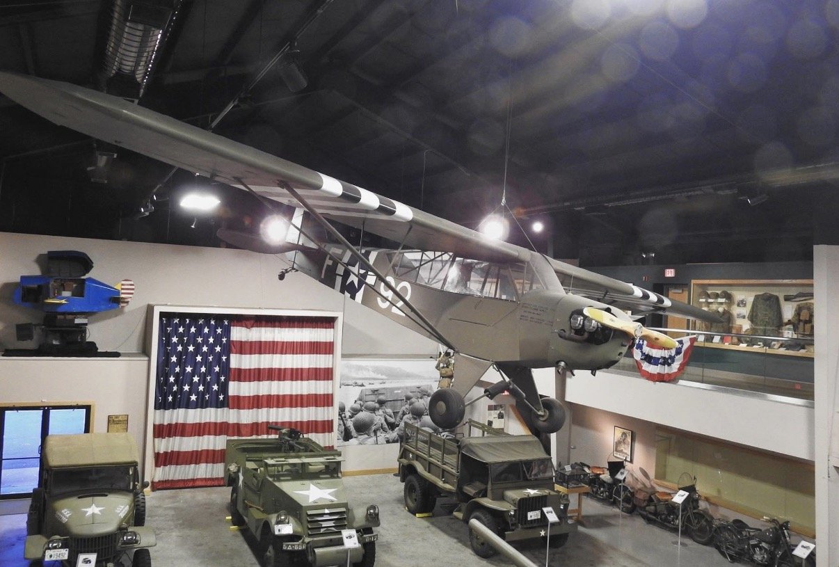 Aircraft suspended above military exhibits and an American flag.