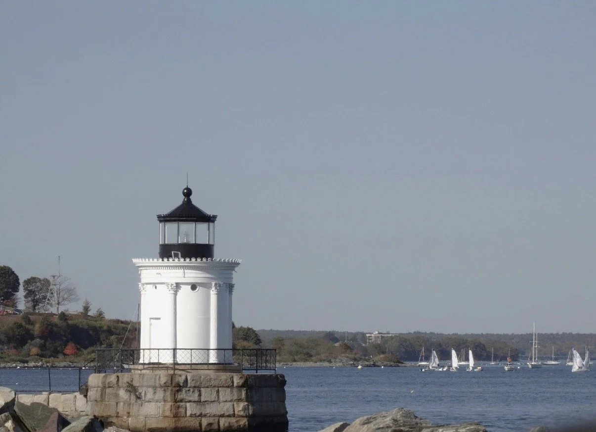 White lighthouse with sailboats in the distance.