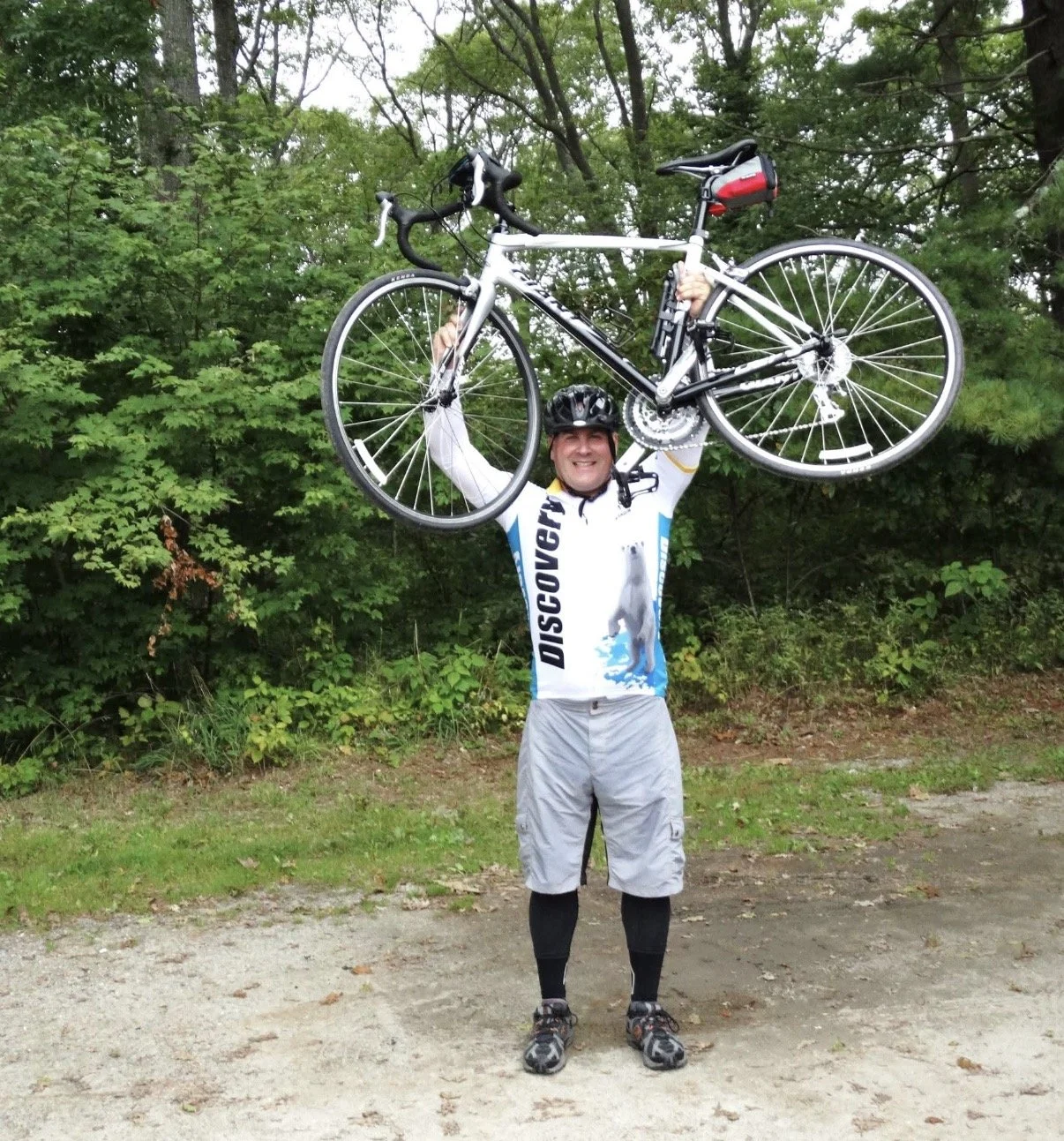 Person holding a bicycle overhead on an outdoor path.