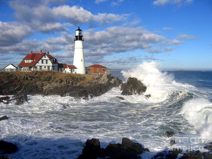 Maine coastal photography — lighthouse and crashing waves beneath a blue sky.