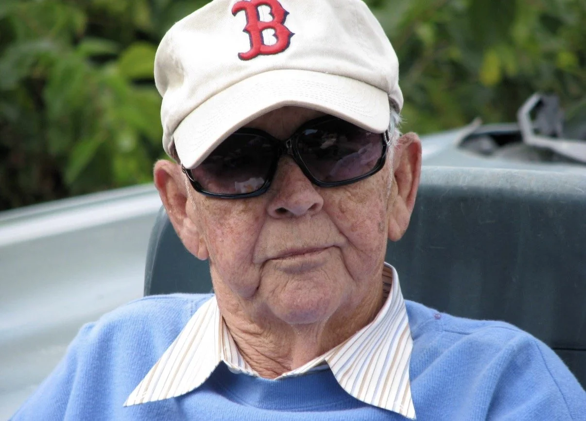 Person wearing sunglasses and a white baseball cap with a red B.