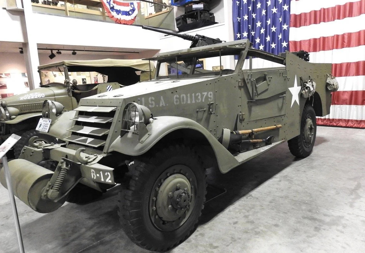 Olive green military vehicle displayed beneath an American flag.