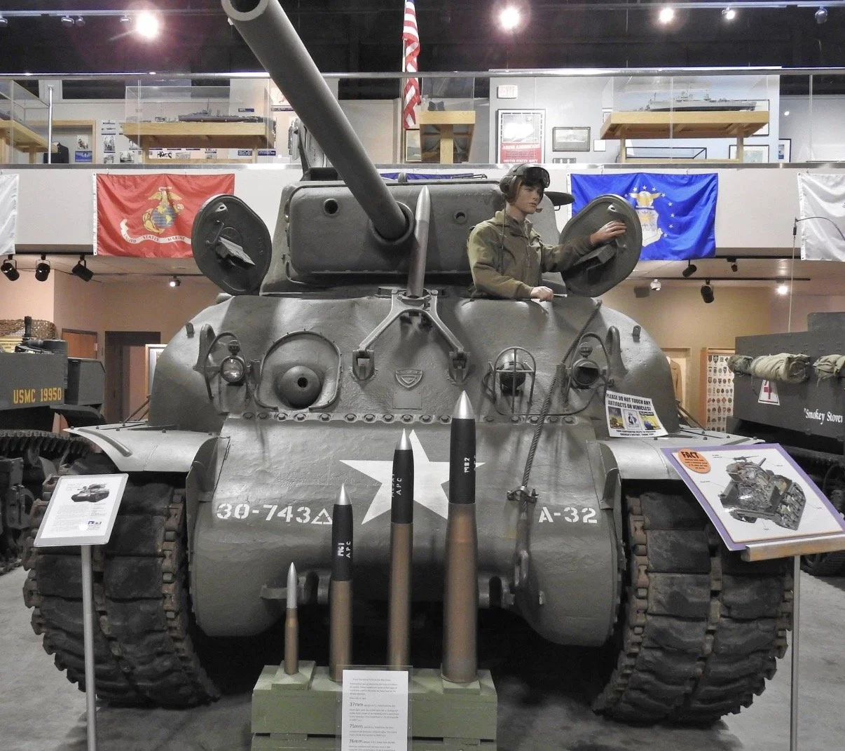 Military tank on display indoors with a seated figure.