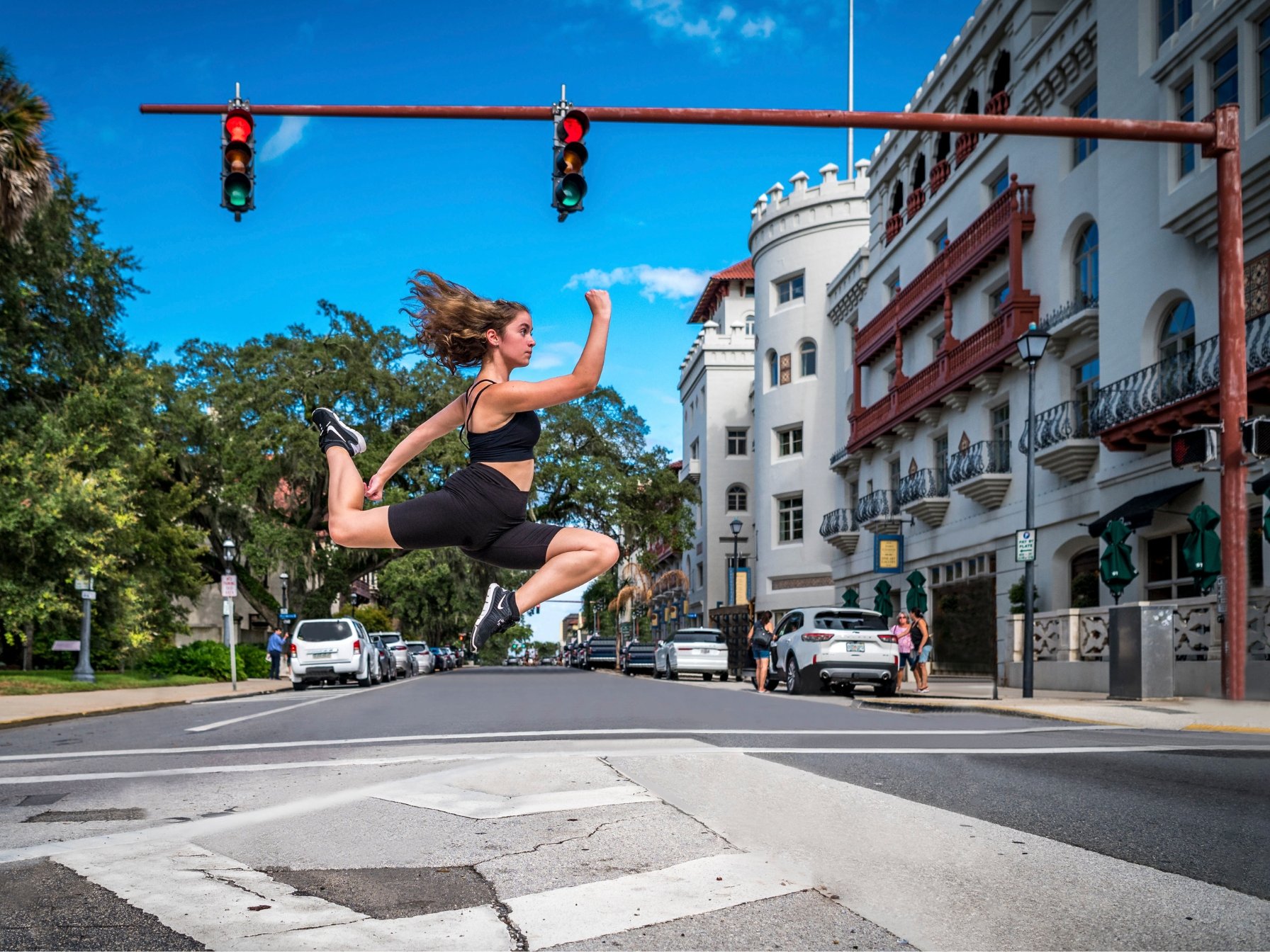 A person in athletic wear performing a mid-air leap on an urban street, with a historic-style building in the background and a traffic light overhead.