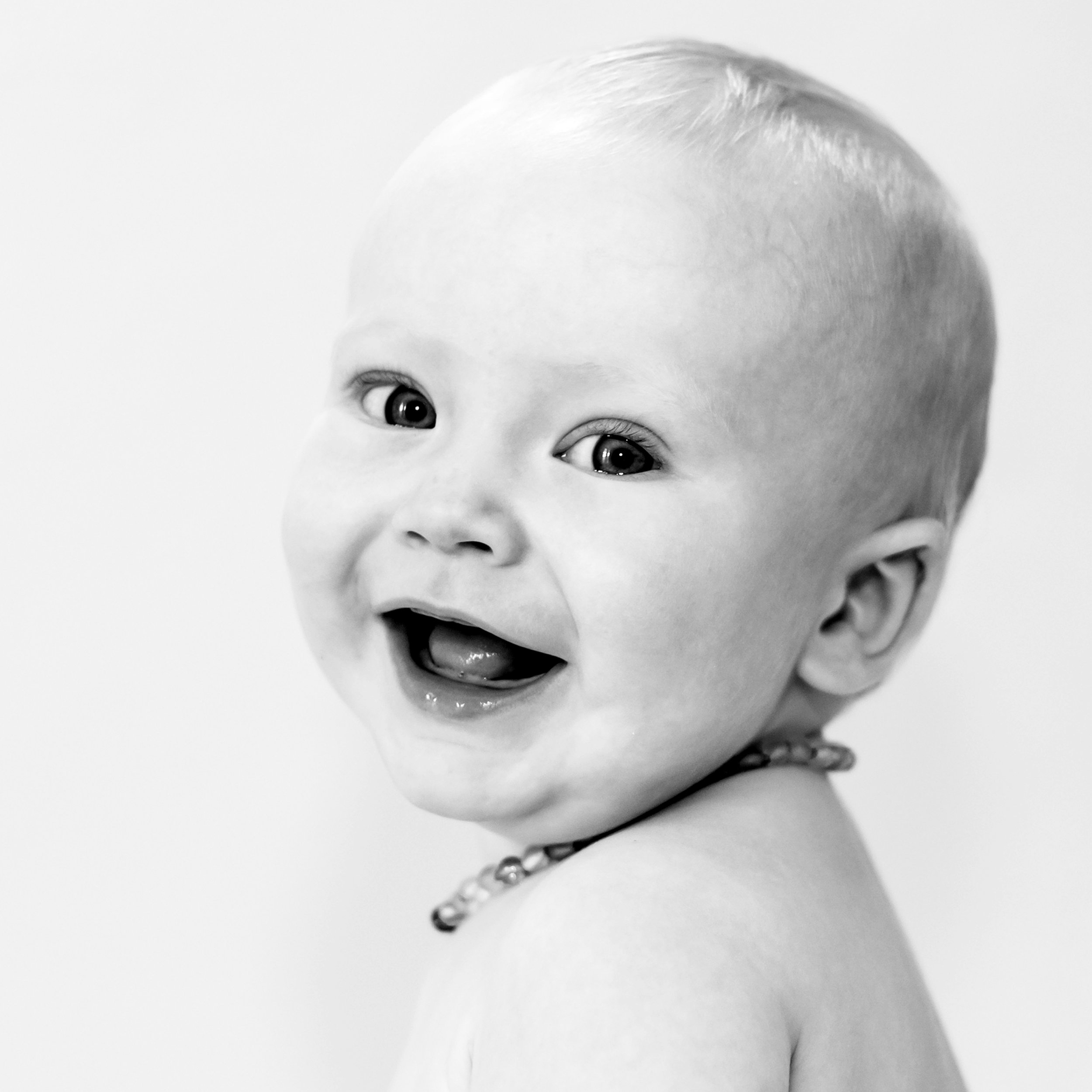 Black and white portrait of a smiling baby wearing a beaded necklace.
